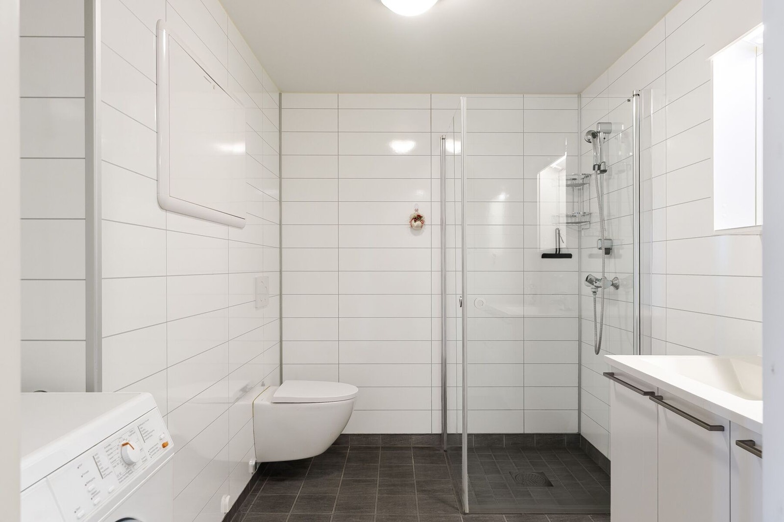 Badet byr på vegghengt toalett, dusjhjørnet, servant og servantskap samt opplegg for vaskemaskin. Galleribilde