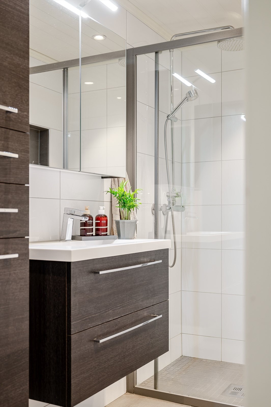 Baderomsinnredning med skuffer og heldekkende servant med ett-greps blandebatteri. I overkant er det speilskap med lys. I tillegg er det et praktisk veggskap. Galleribilde