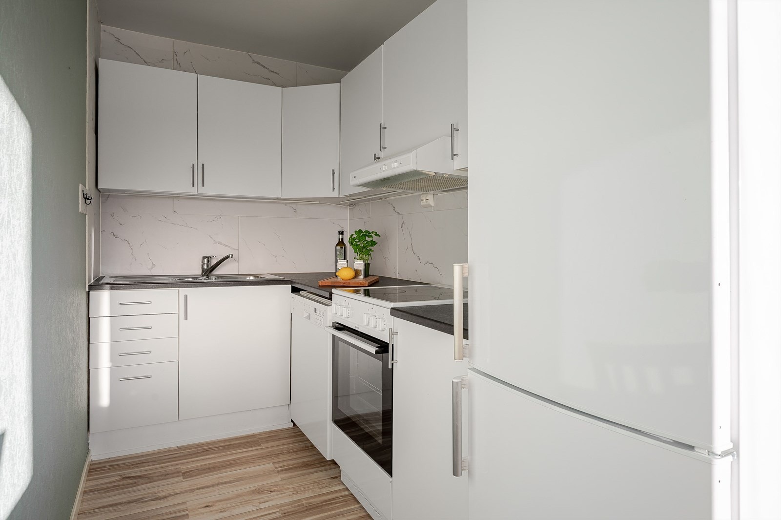 Lyst kjøkken med innredning med hvite, glatte fronter. Galleribilde