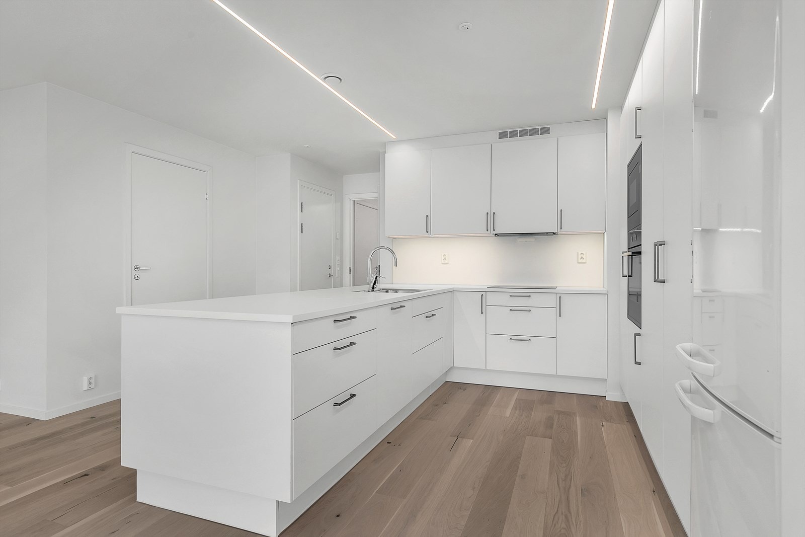 Med integrerte hvitevarer, god benkeplass og oppbevaringsmuligheter kombinerer kjøkkenet estetikk og praktisk bruk på en sømløs måte. Galleribilde