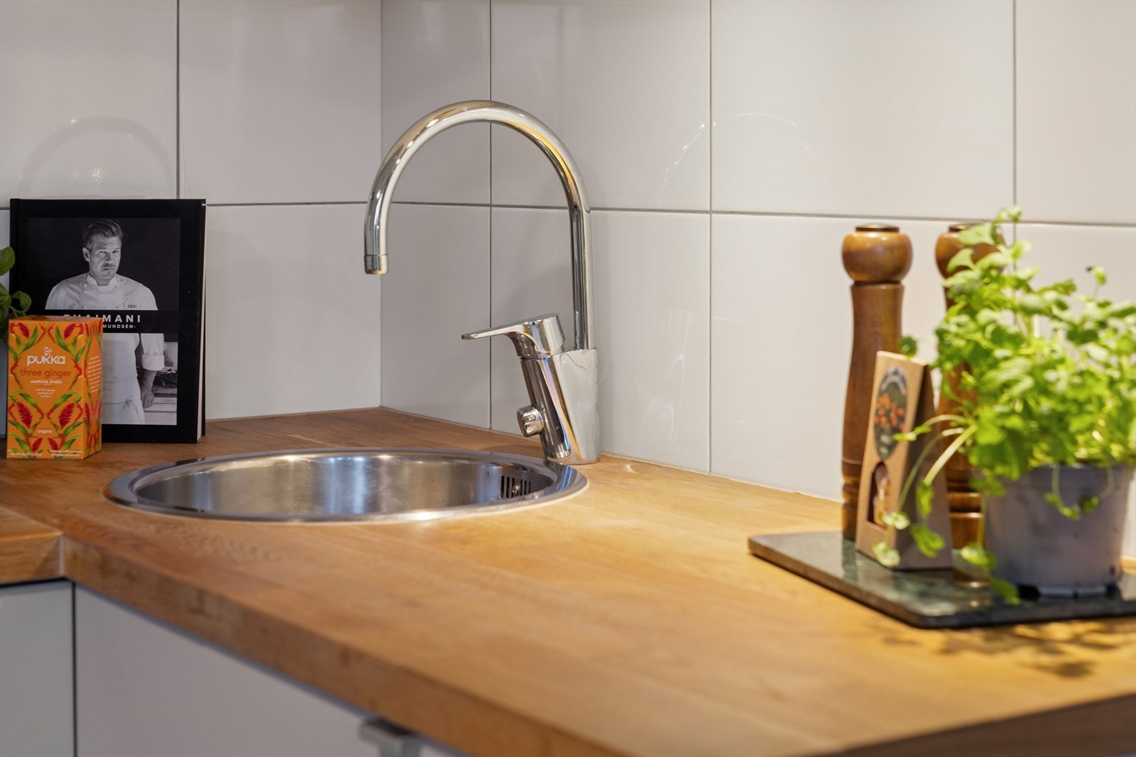 Slette lakkerte fronter, laminat benkeplate m/fliser over, enkel oppvaskkum, kjøkkenventilator i stål, integrert koketopp, stekeovn og oppvaskmaskin, samt frittstående kjøl-/fryseskap. Galleribilde