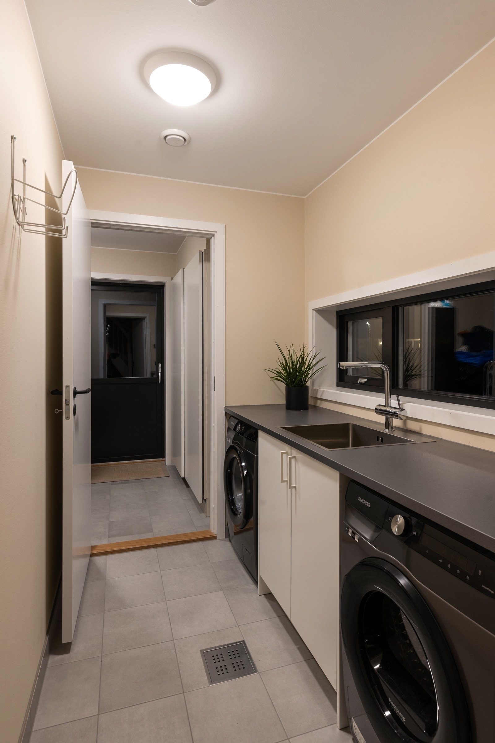 Vaskerom med innrending. Stor bod med dør ut innenfor vaskerom. Fliser på gulv i begge rommene. Galleribilde