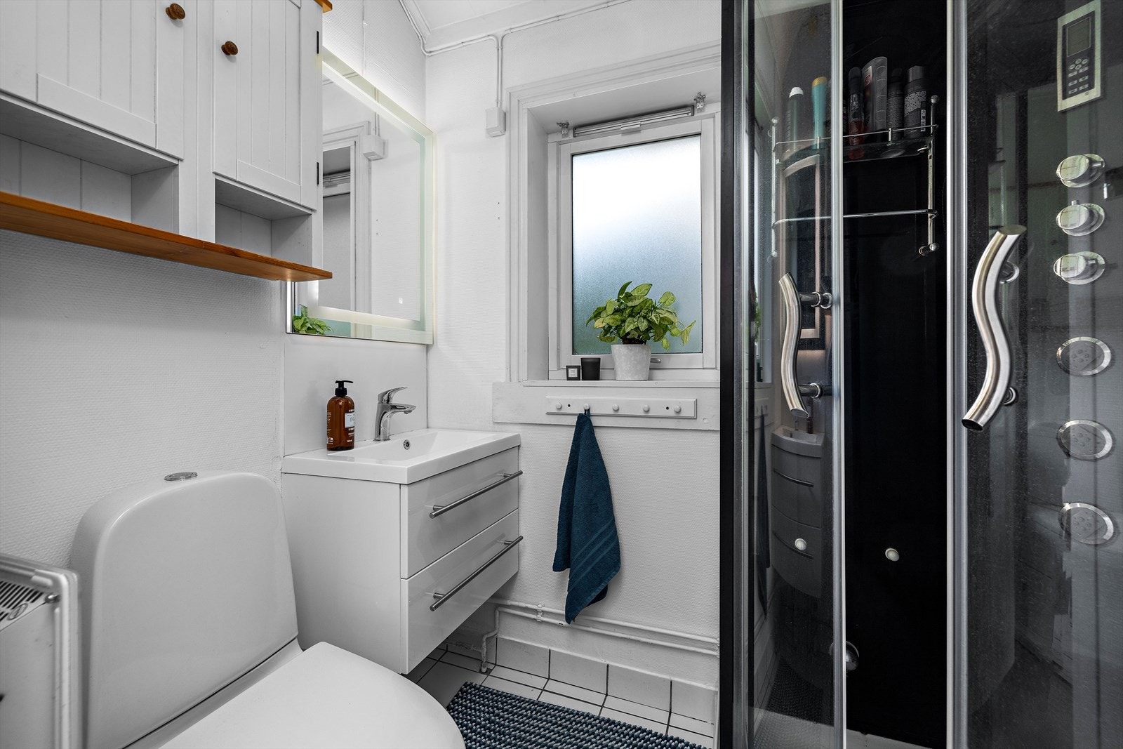 Badet har flislagt gulv og er innredet med dusjkabinett, servantinnredning og toalett. Galleribilde