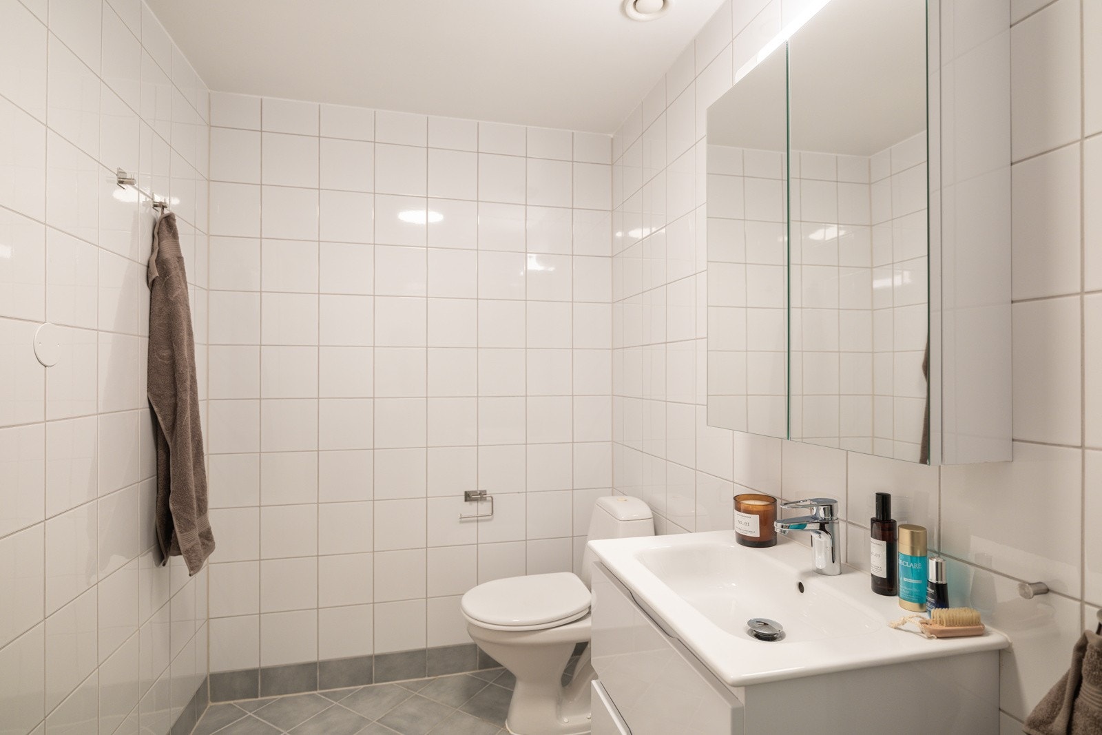 Moderne baderomsinnredning med skuffer og heldekkende servant, speilskap med belysning over. Baderommet er også utstyrt med dusjhjørne med innfellbare glassdører og gulvstående toalett. Galleribilde