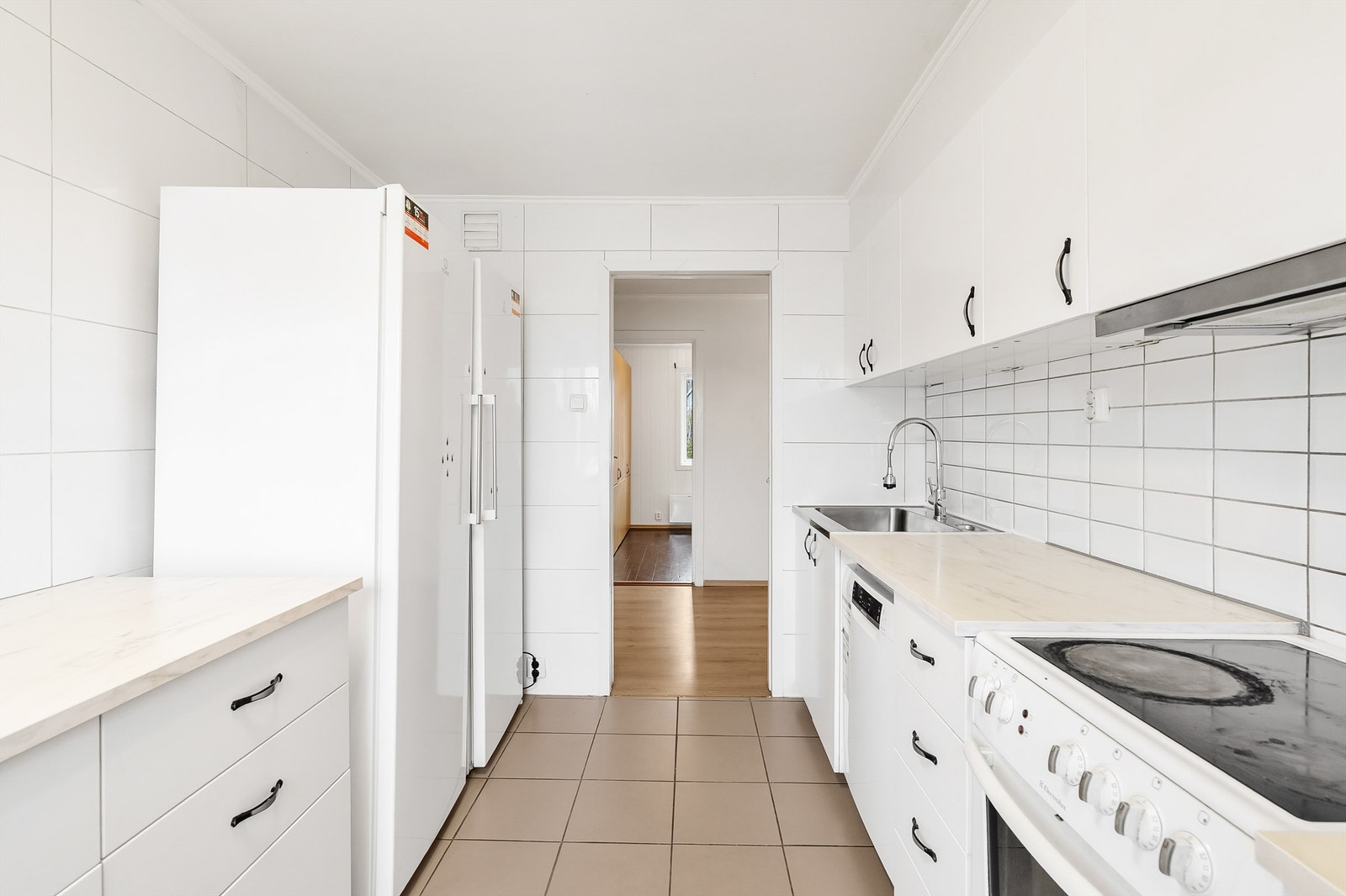 Kjøkkenet er innredet med frittstående kjøleskap, fryseskap, oppvaskmaskin og komfyr Galleribilde