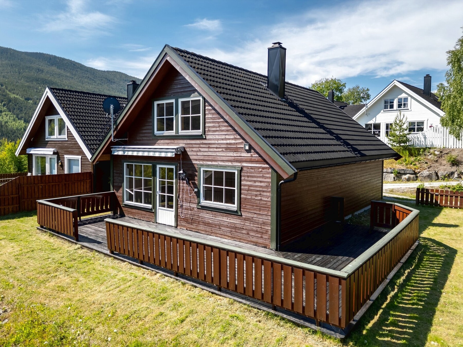 Foto av boligen i sommersesong, med utgang til terrasse og videre adkomst til terreng. Eiendommen byr på flat plen og gode utearealer med mange bruksmuligheter. Galleribilde