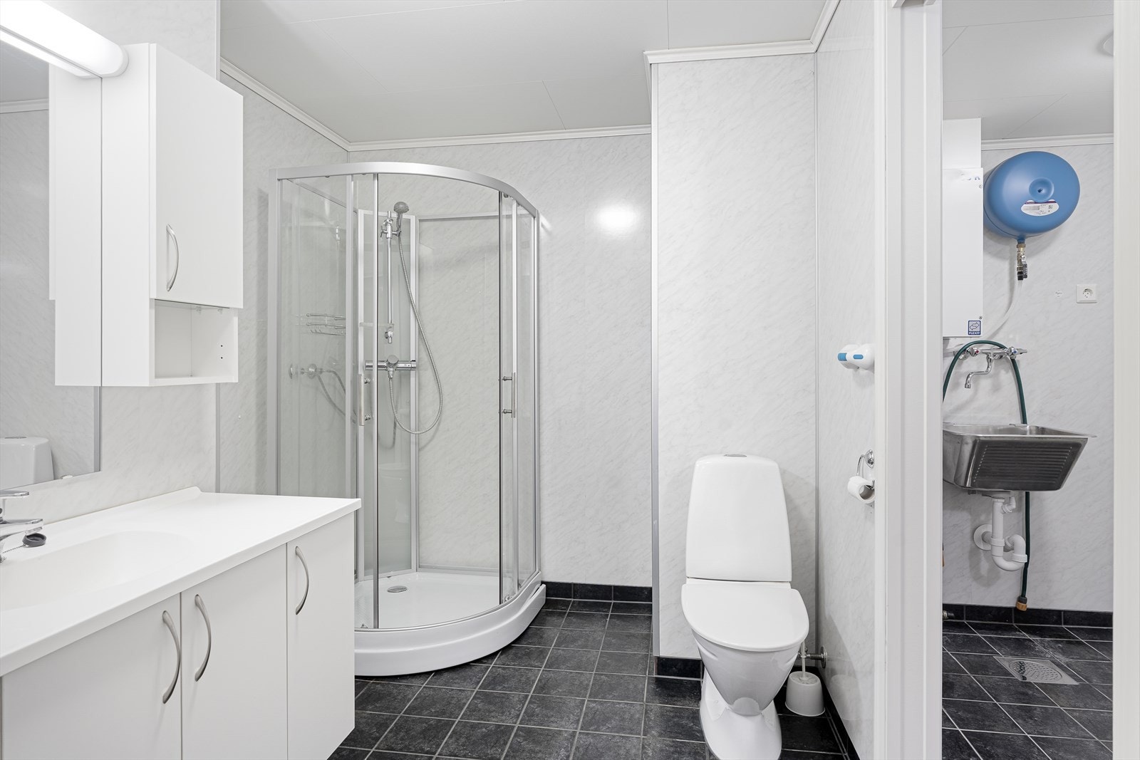 Praktisk baderom med fliser på gulv. Innredet med wc, vask i seksjon og dusj. Galleribilde