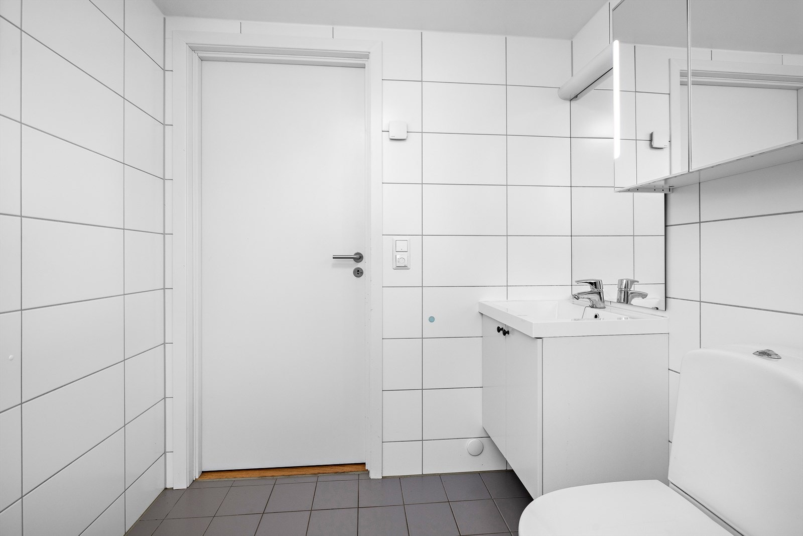 Badet er innredet med servantskap, speilskap, toalett og et dusjhjørne med innfellbare glassdører. Galleribilde