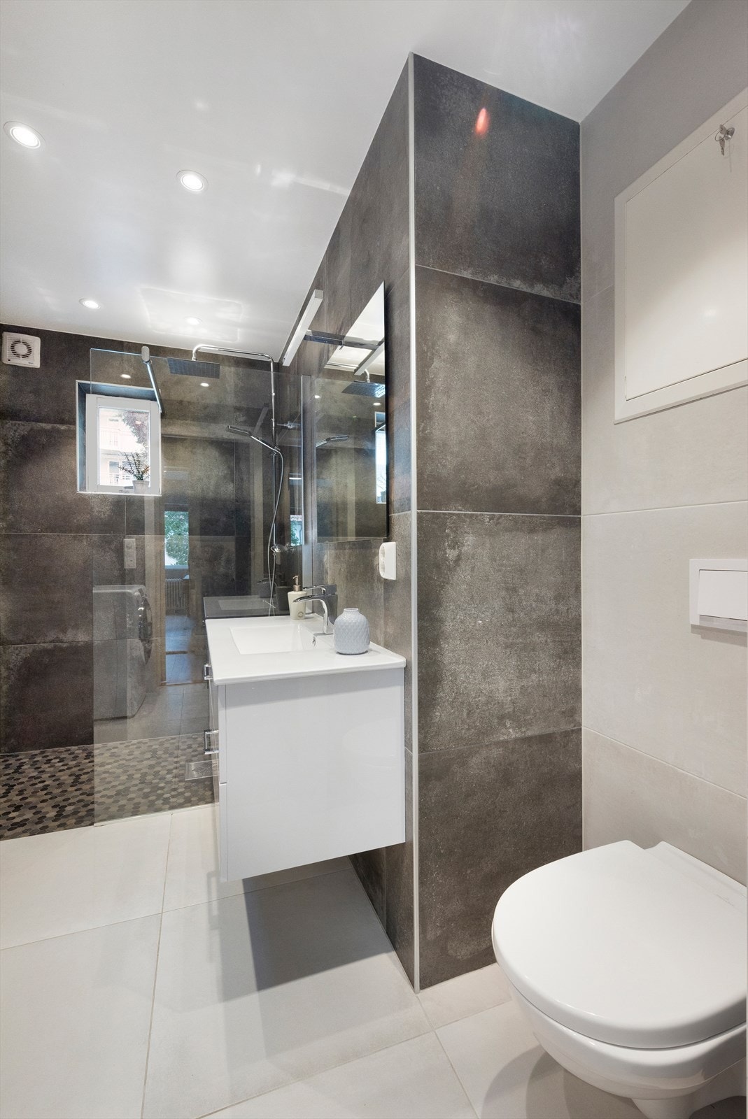 Badet er utstyrt med opplegg for vaskemaskin, rørfordelingsskap, servantskap, mekanisk avtrekk, dusjhjørne og veggmontert wc Galleribilde