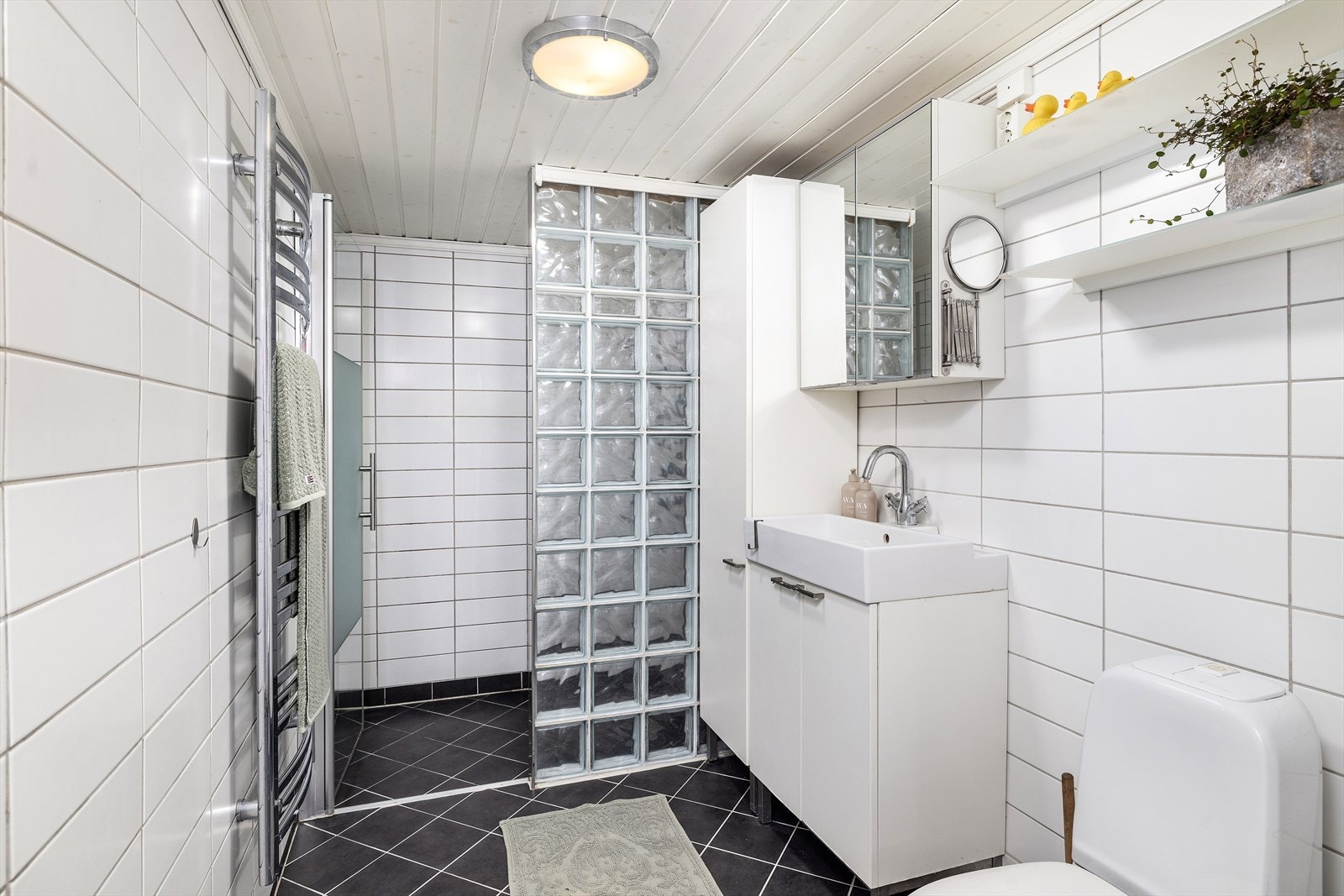 Flislagt bad med varmekabler i gulv, enkel servantinnredning, toalett og dusj. Galleribilde