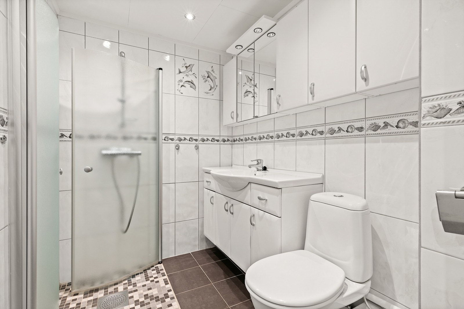 Pent flislagt bad med varmekabler i gulvet.
Innredningen består av skap med glatte fronter, dusjhjørne, servant og klosett Galleribilde