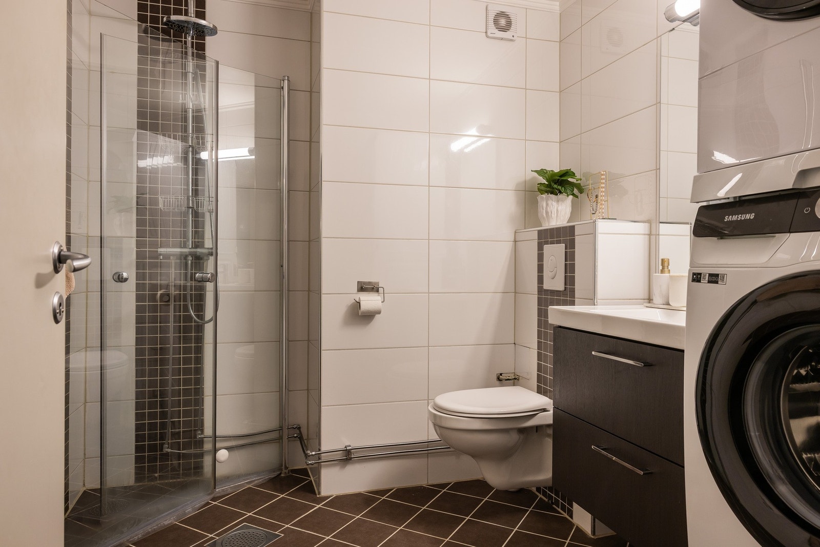 Pent flislagt bad med dusjnisje med innfellbare dusjdører, servant med ett greps blandebatteri og vegghengt toalett. Galleribilde