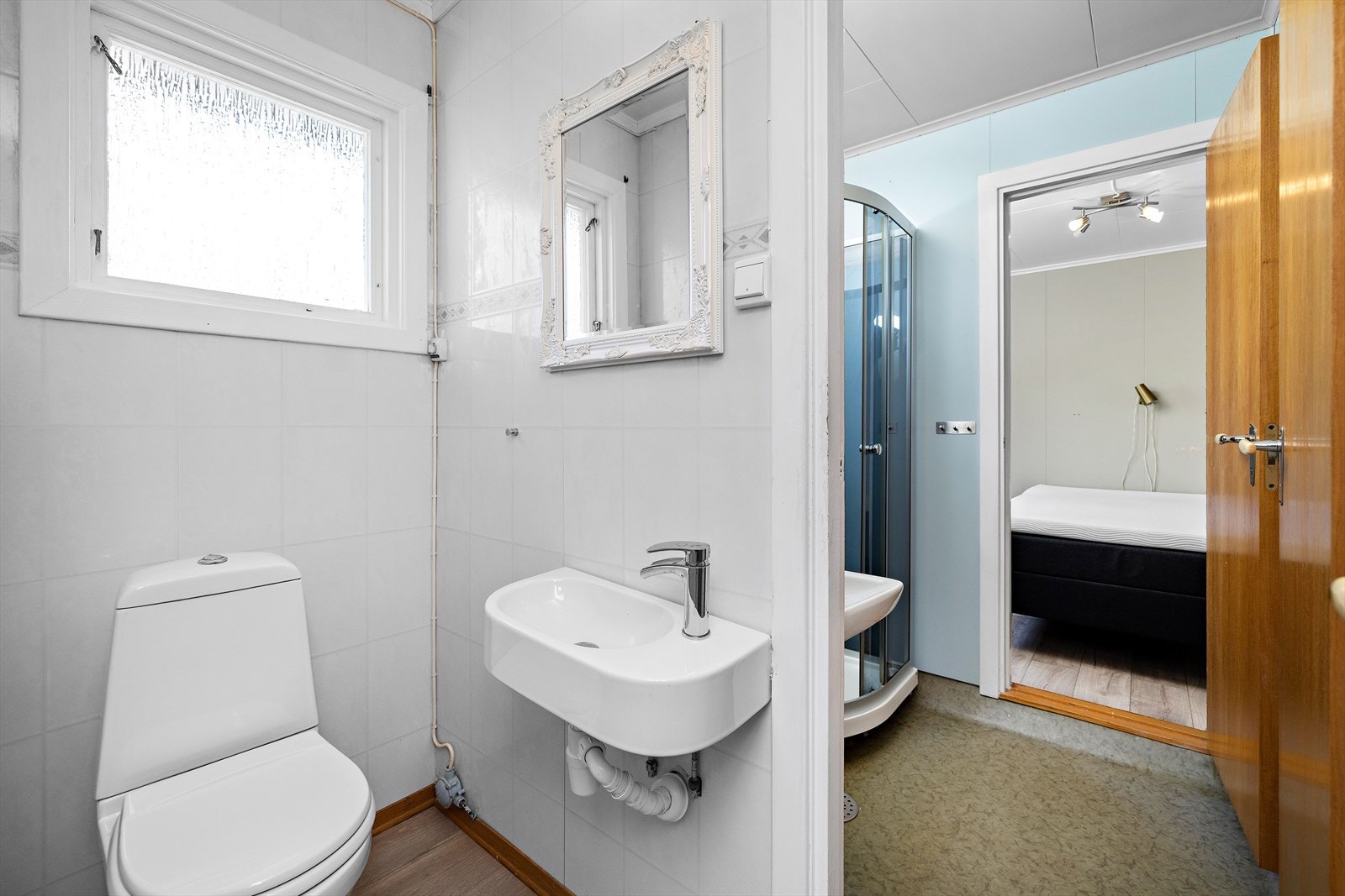 Bad med baderomsplater og vinylbelegg, dusjkabinett og servant. Toalettrom ved siden av. Galleribilde