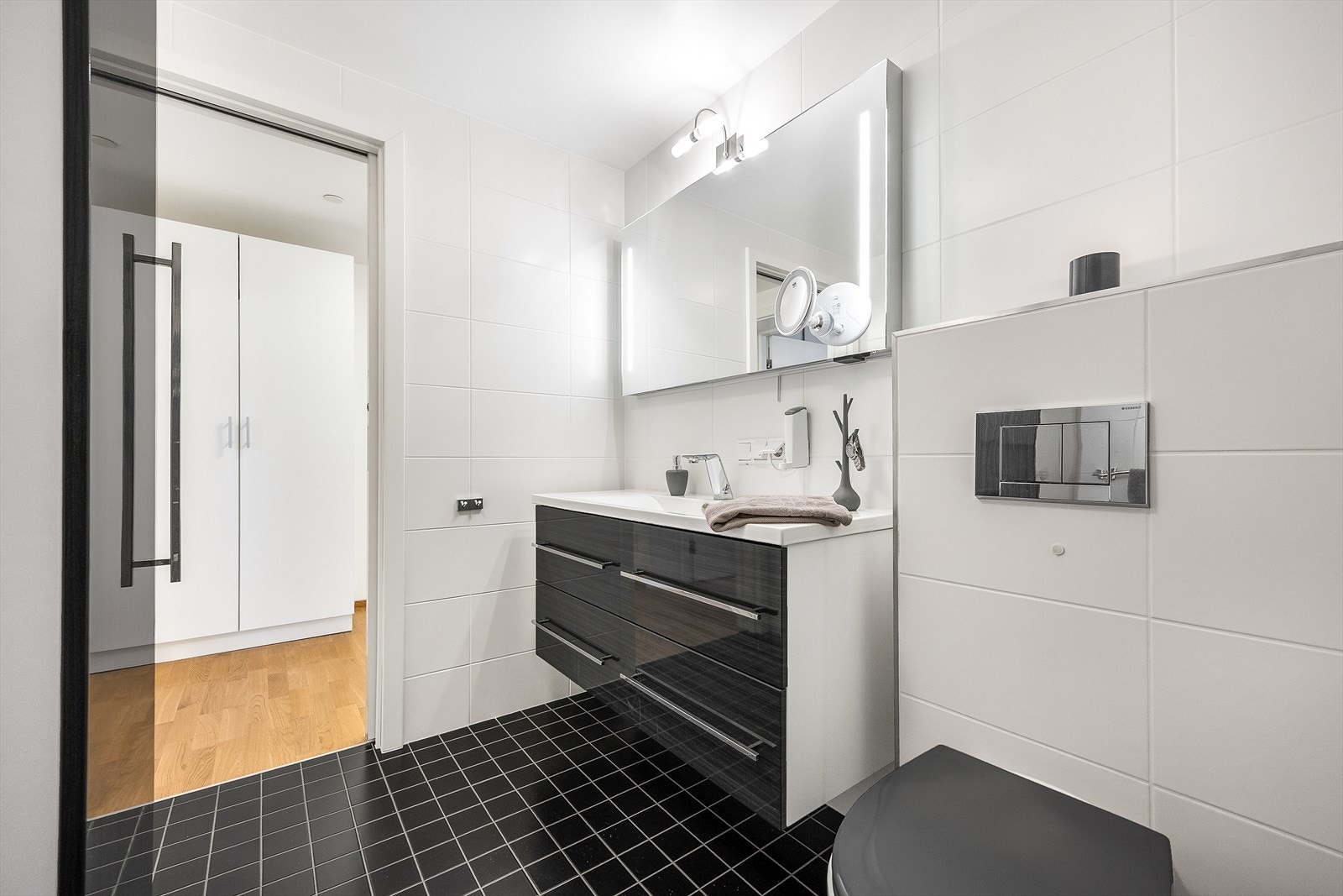 Badet er innredet med servant i baderomsinnredning med speil med integrert belysning over, vegghengt toalett, stor dusjnisje og ekstra vegghengt skap. Galleribilde