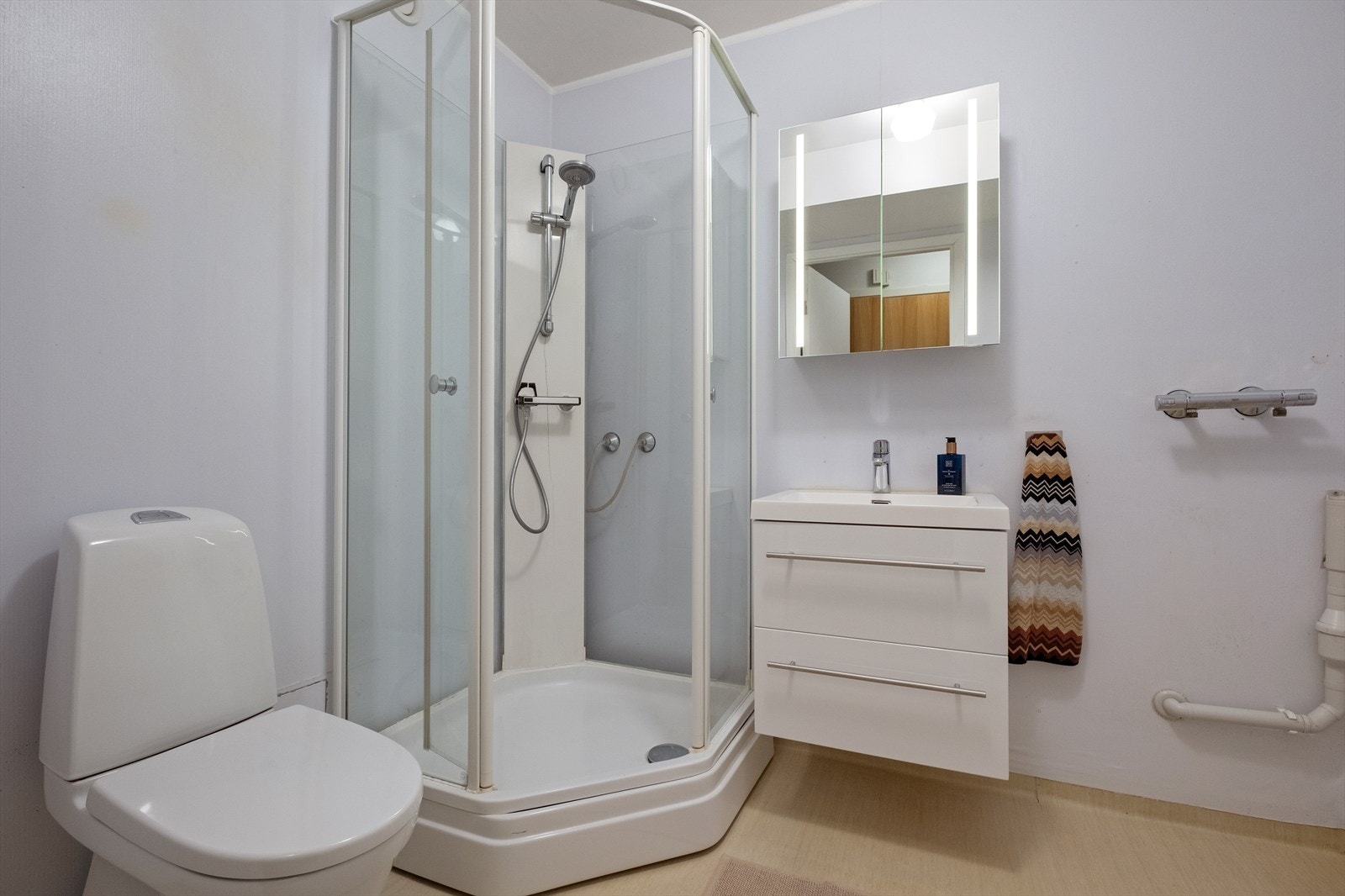 Bad med dusjkabinettet med blandebatteri, gulvstående wc og servantskap med skuffer. Galleribilde