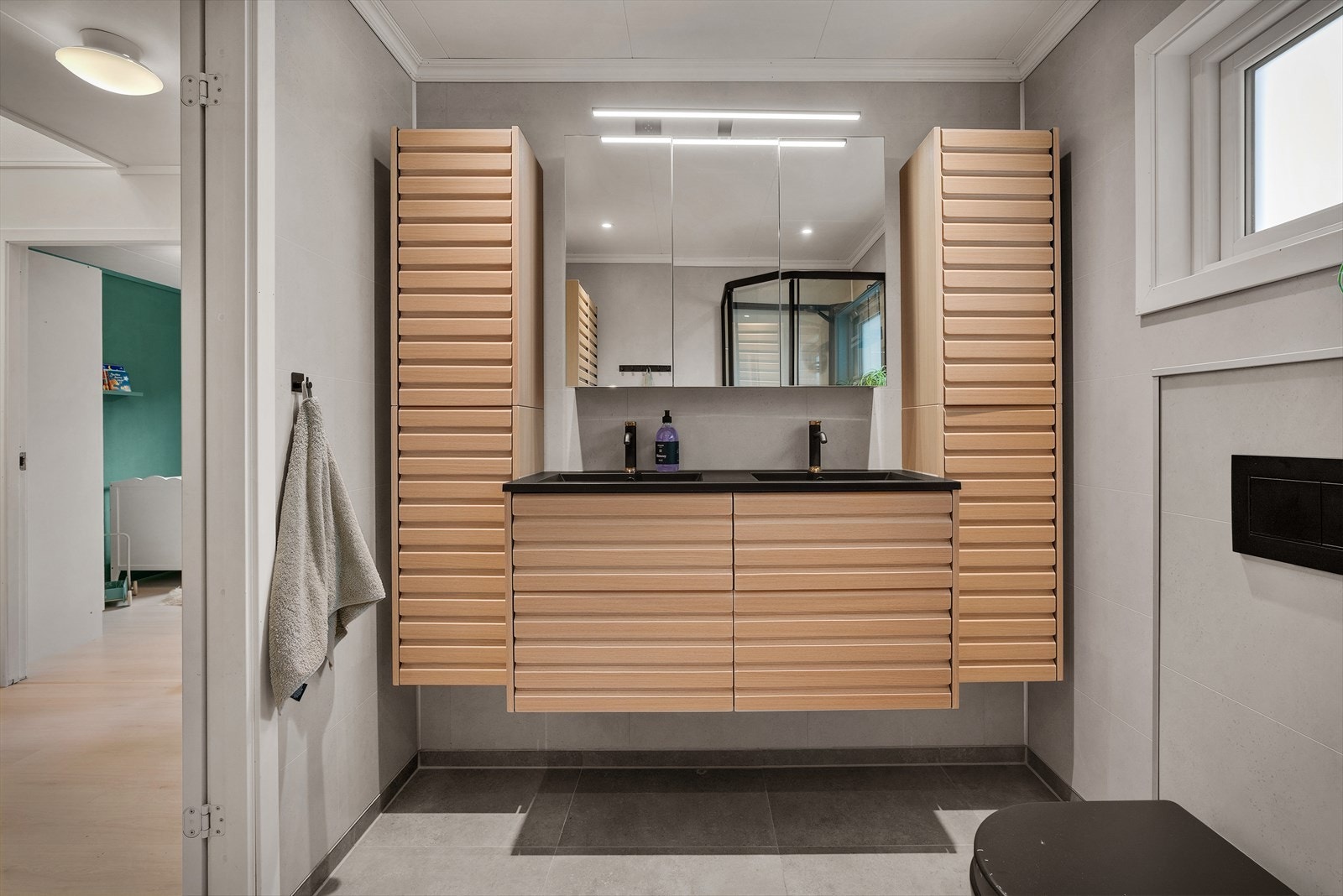 Her er flislagt gulv, våtromsplater på veggene, dusjkabinett, veggmontert toalett og dobbel servant med god oppbevaringsplass Galleribilde