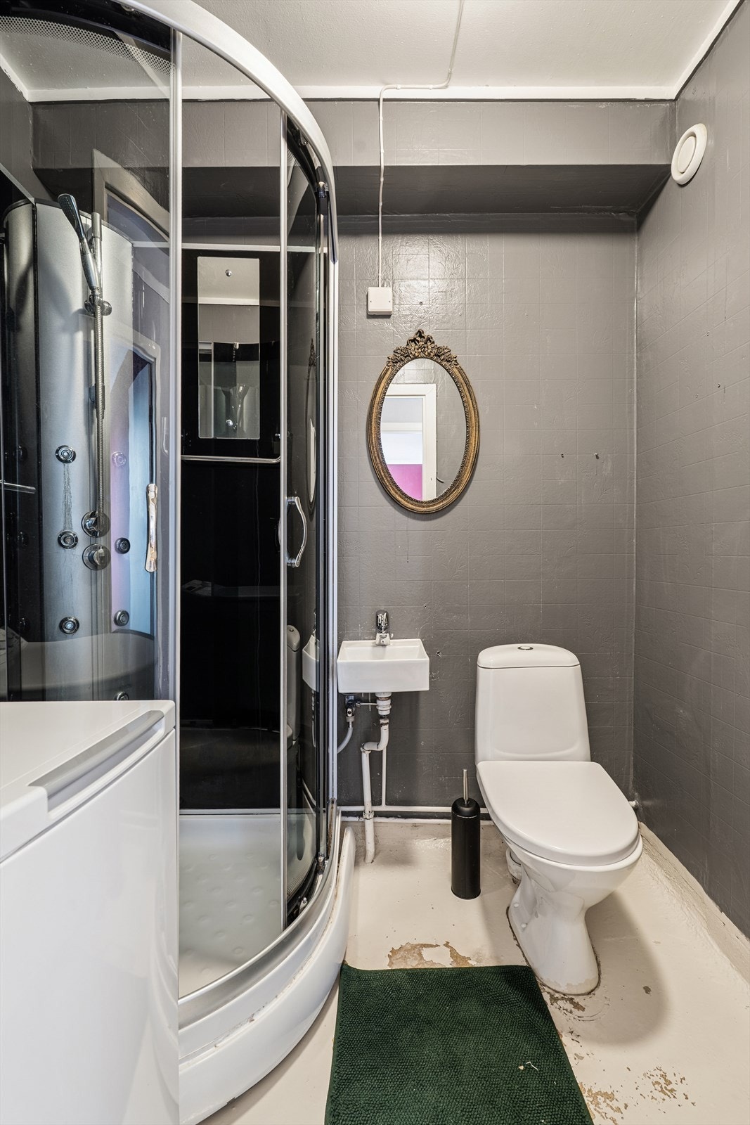 Badet er utstyrt med klosett, liten servant, dusjkabinett og røropplegg til vaskemaskin. Badet er av eldre dato og rehabilitering bør prioriteres for å sikre tilfredsstillende funksjon og hindre videre forringelse. Galleribilde