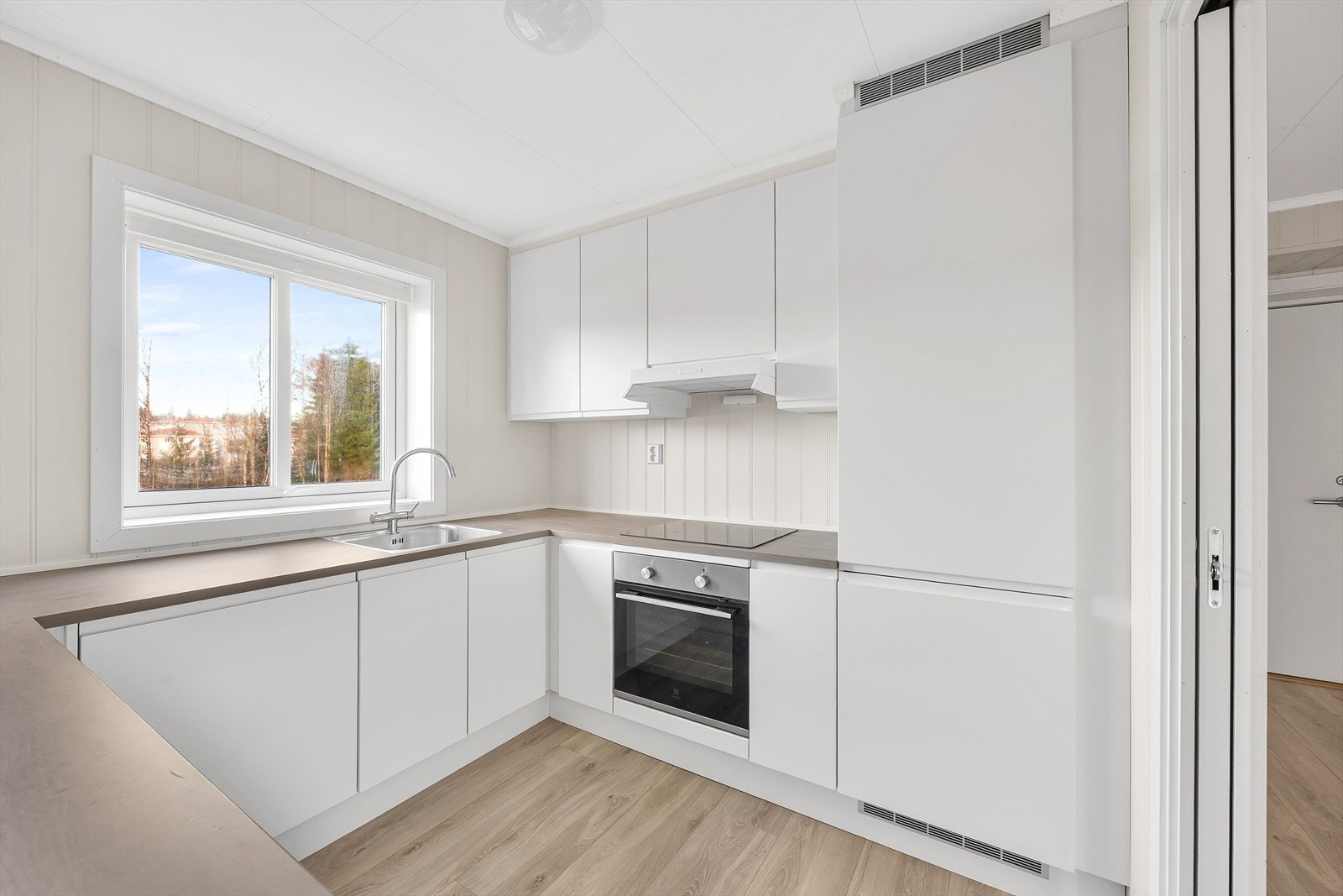 Kjøkkeninnredningen har glatte, hvite fronter og en slitesterk laminatbenkeplate. Galleribilde