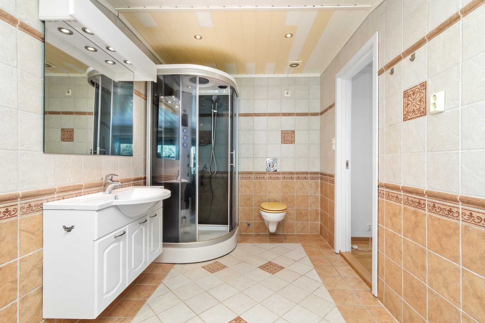 Badet har varme i gulv og er innredet med servant over servantskap med profilerte fronter, vegghengt toalett og dusjkabinett. Galleribilde