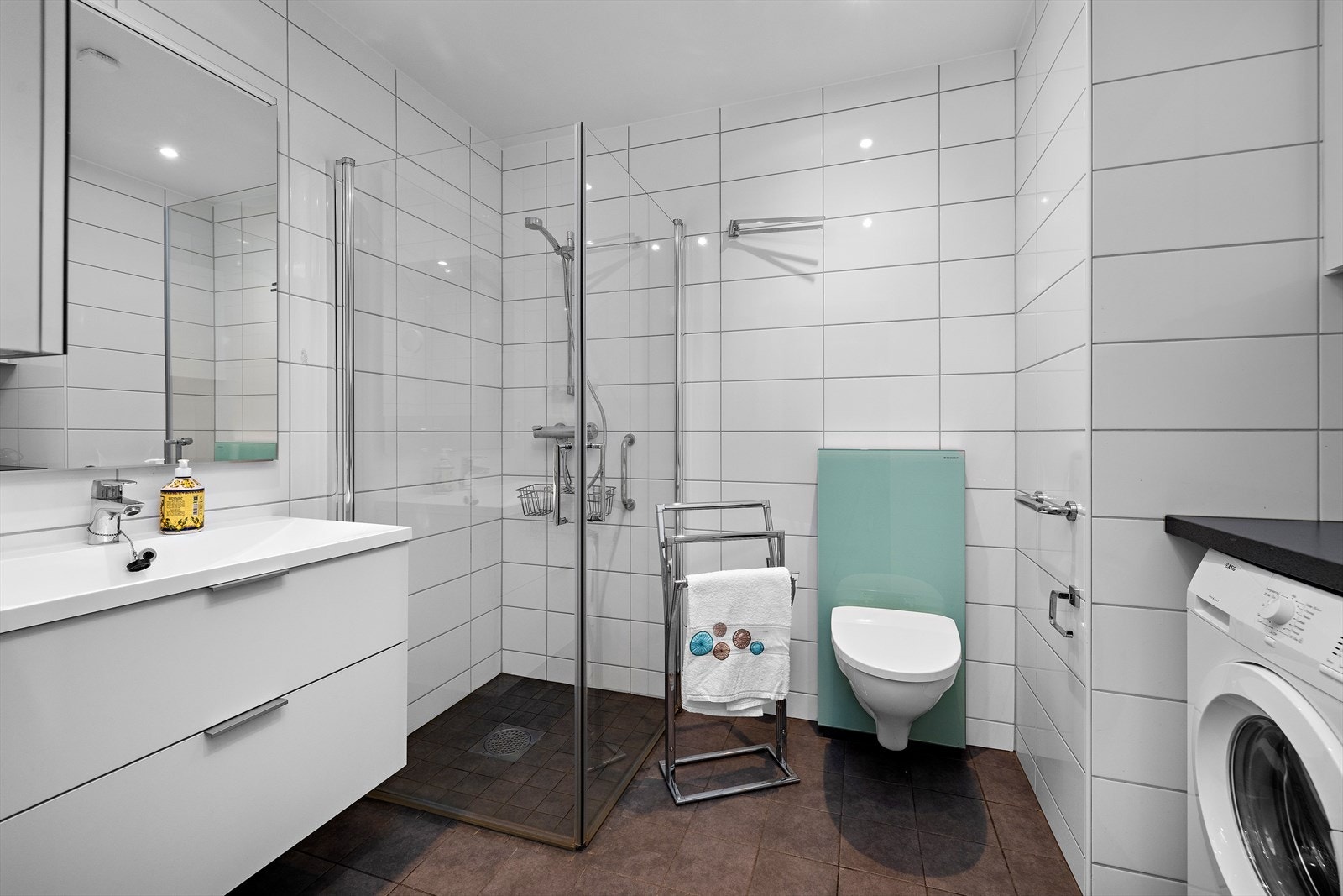 Flislagt bad kombinert med vaskerom. Det er innredet med dusjhjørne og en praktisk vaskeromsinnredning med opplegg for vaskemaskin. Galleribilde