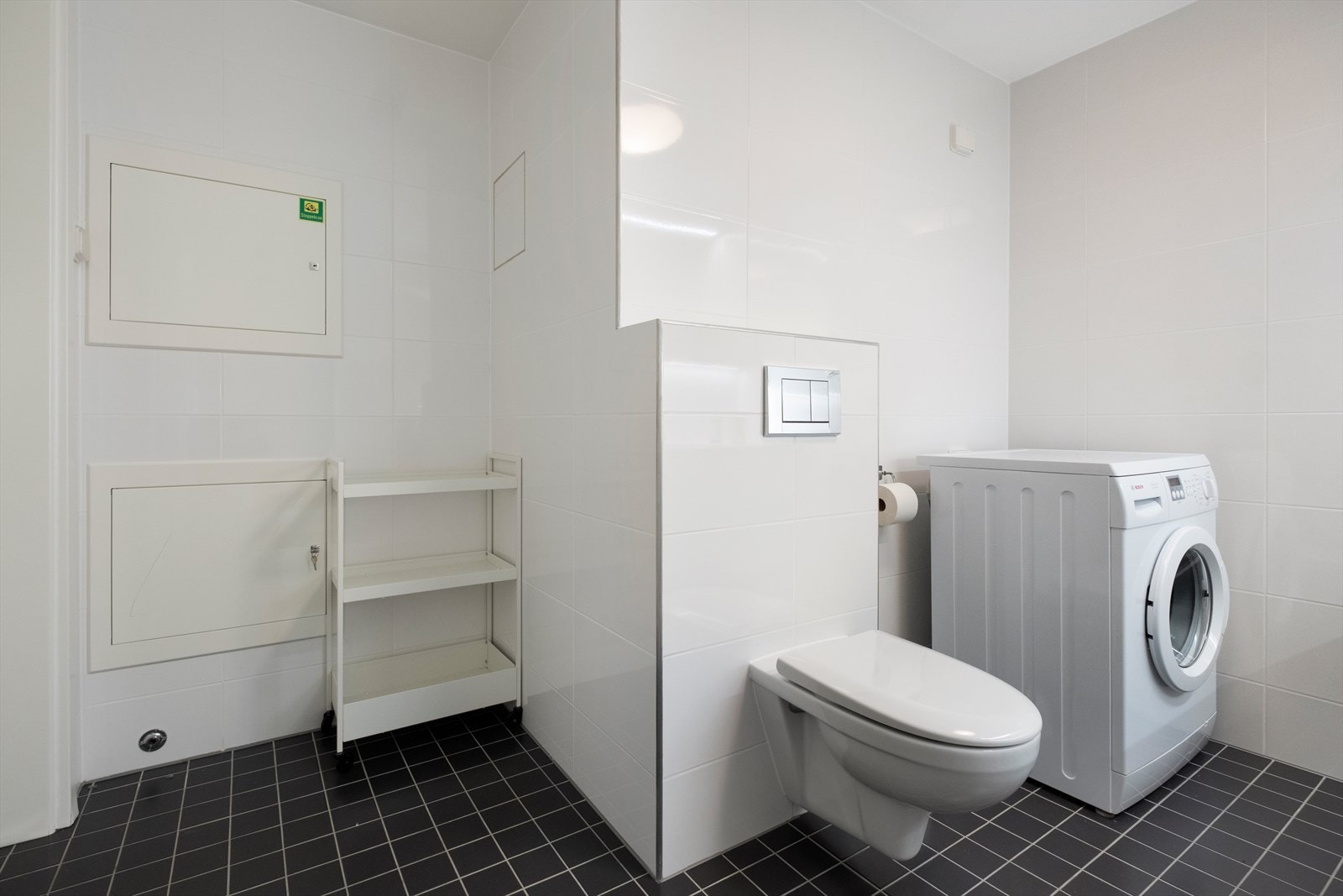 Badet er utstyrt med heldekkende servant, speilskap over servant, vegghengt toalett, dusjvegger av glass og opplegg for vaskemaskin Galleribilde