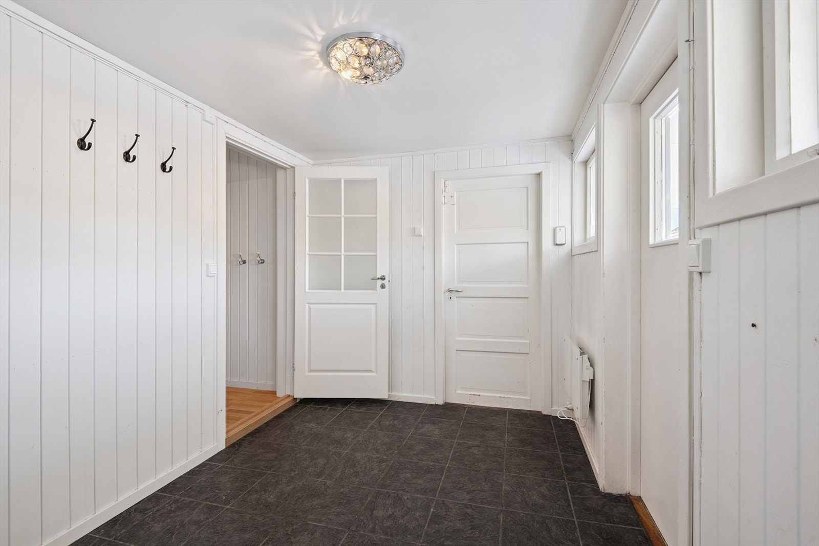 Vi starter i første etasje. En lys entré med panelvegger og praktisk flislagt gulv. Herfra er det adkomst ned til felles kjeller. Galleribilde