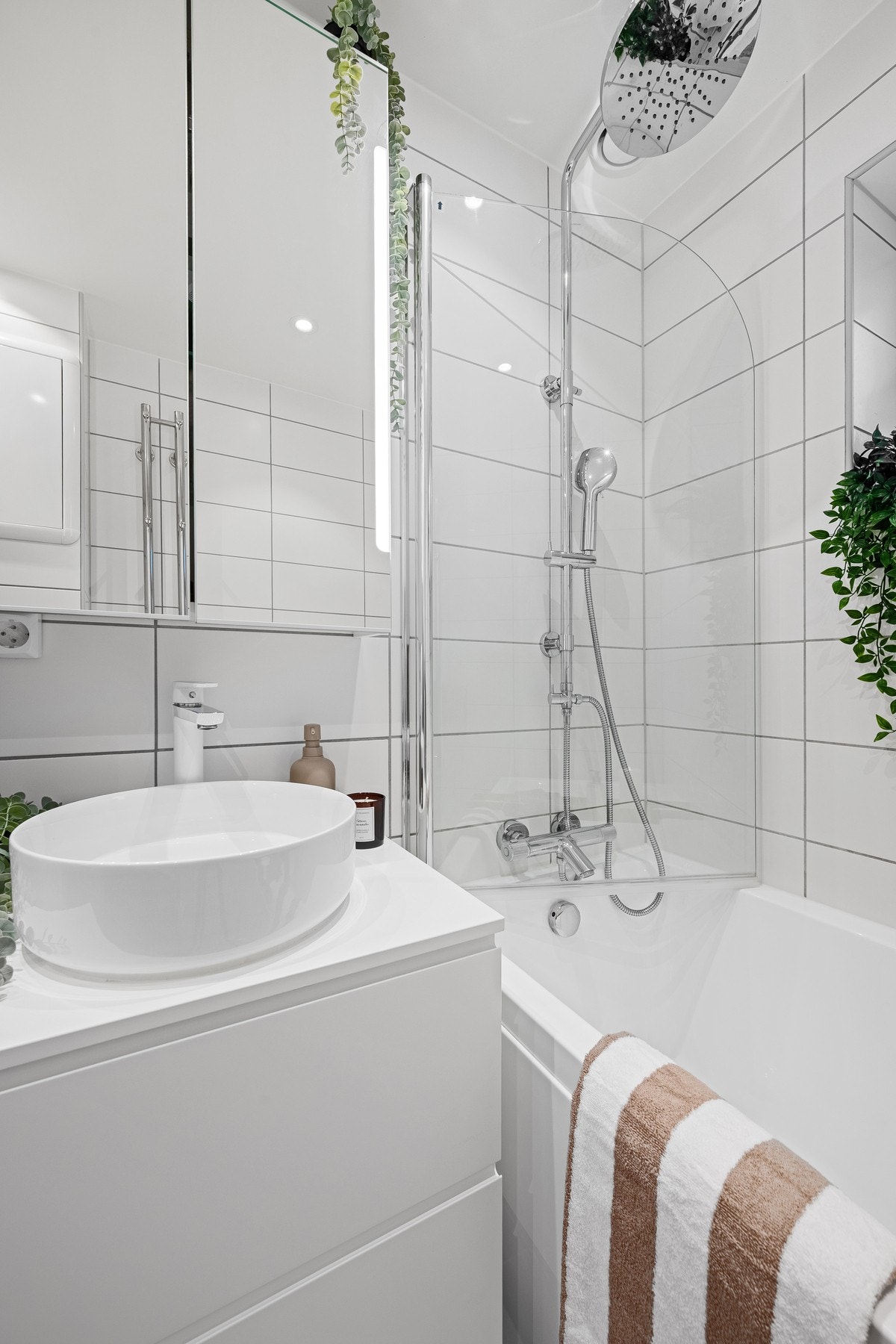 Baderommet fremstår som moderne og funksjonelt, med flislagte gulv og vegger samt et slett, hvitmalt tak. Galleribilde