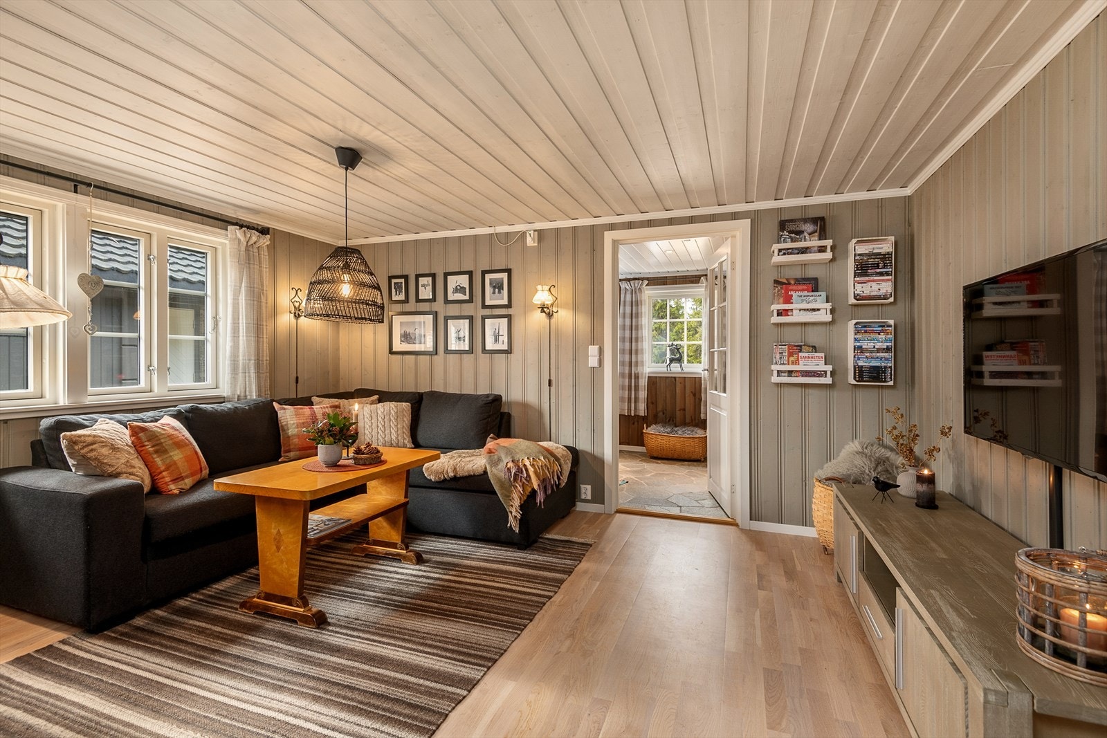 Den hyggelige stua har beiset panel på både på tak og vegger. Nytt gulv er lagt i senere år. God plass til å møblere med sofa. Galleribilde