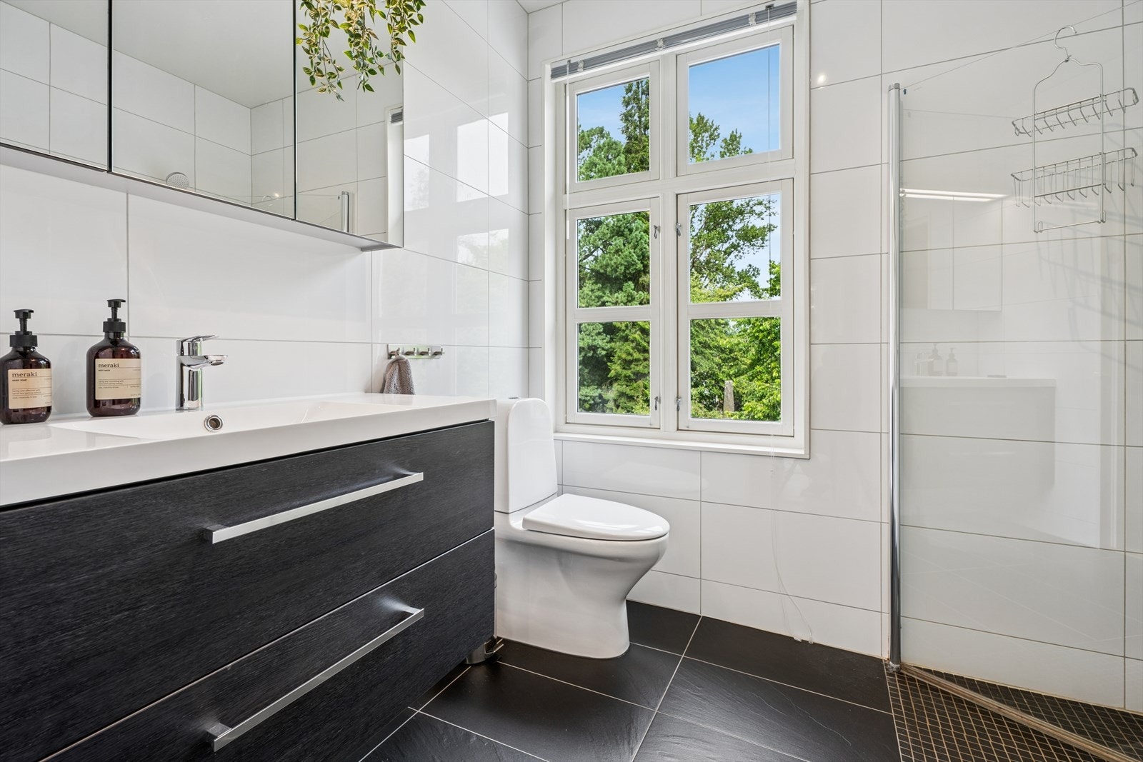 Baderomsinnredningen inkluderer speilskap, porselensvask med etgrepsarmatur, gulvmontert toalett og elektrisk tørkestativ på vegg. Galleribilde