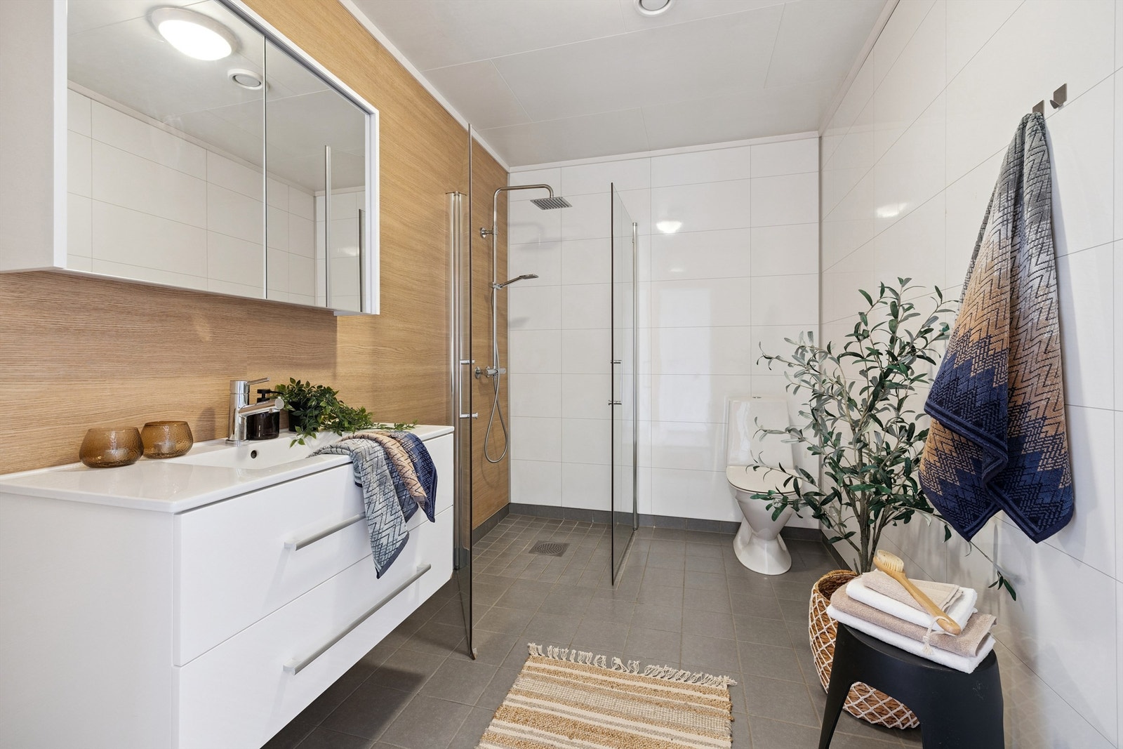 Flislagt bad med vegghengt toalett, dusjhjørne og servant med skuffeseksjon. Galleribilde