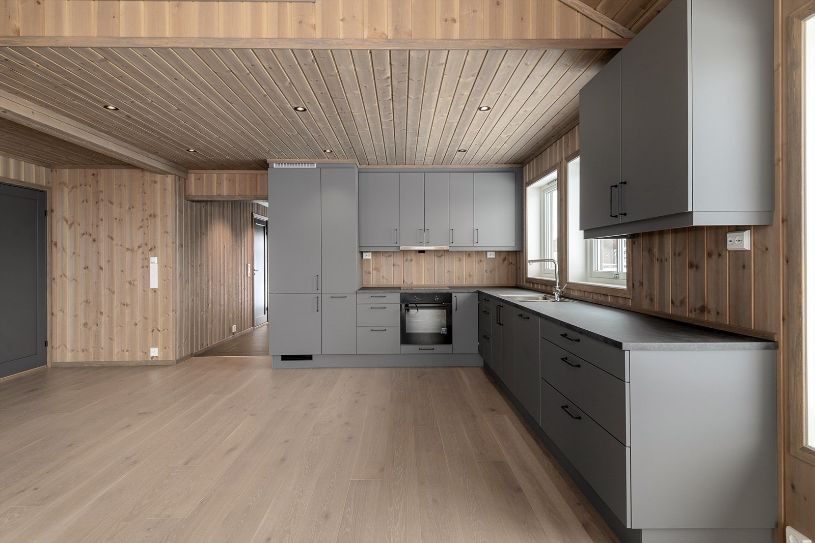 Romslig kjøkkeninnredning i en grå, elegant fargetone. Stramme, glatte fronter med integrerte hvitevarer. Det er rikelig med både skap-og benkeplass på kjøkkenet. Galleribilde