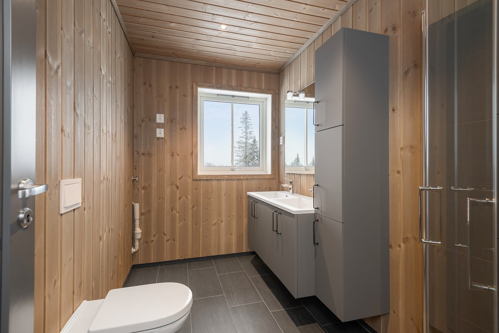 Hytta har to, fine og funksjonelle bad. Dette badet har fliser på gulv i dusjsonen. Innfellbare dusjvegger i glass. Øvrige vegger har og tak har behandlet panel. Vegghengt WC. Galleribilde