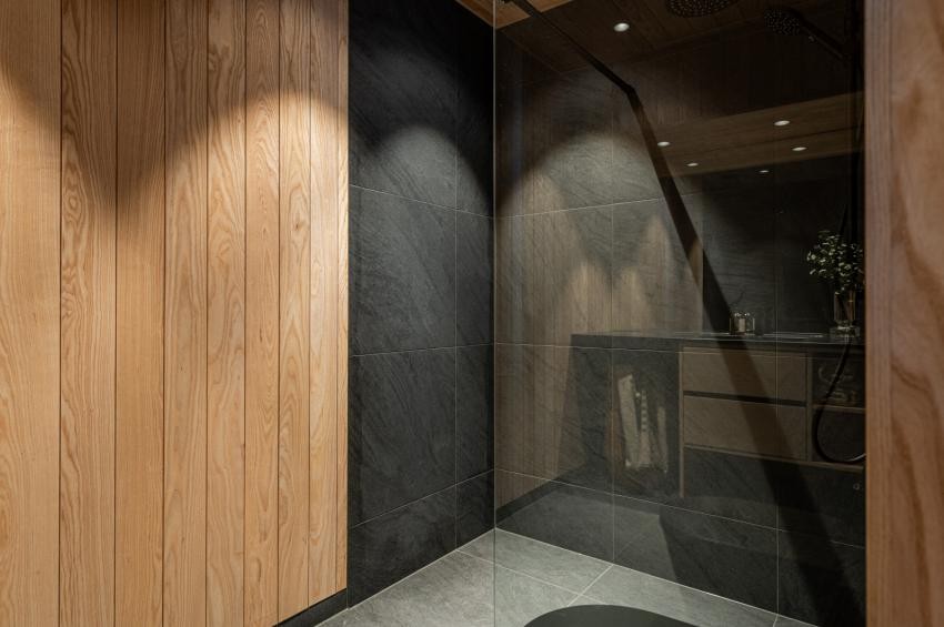 Elektriske varmekabler i flisgulv samt sorte LED downlights med tilbaketrukket lyskilde. (Bilde av en tilsvarende hytte i prosjektet) Galleribilde