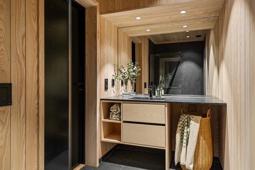 Bilde fra en ferdigstilt (speilvendt) enh. Her ses fliser i fargen Soot (mørk grå), mens det for enhet 13A er valgt Tephra (lysere grå). Møbel i heltre ask og eksklusivt askepanel. Sort servantbatteri, dusjaramtur, dusjprofil samt wc med sort trykkplate. Galleribilde