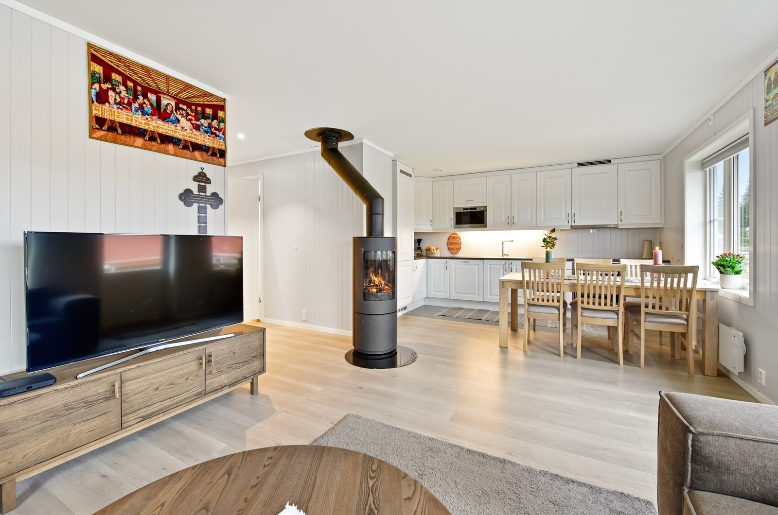 Leiligheten har en åpen stue- og kjøkkenløsning med en sentralt plassert vedovn. Galleribilde