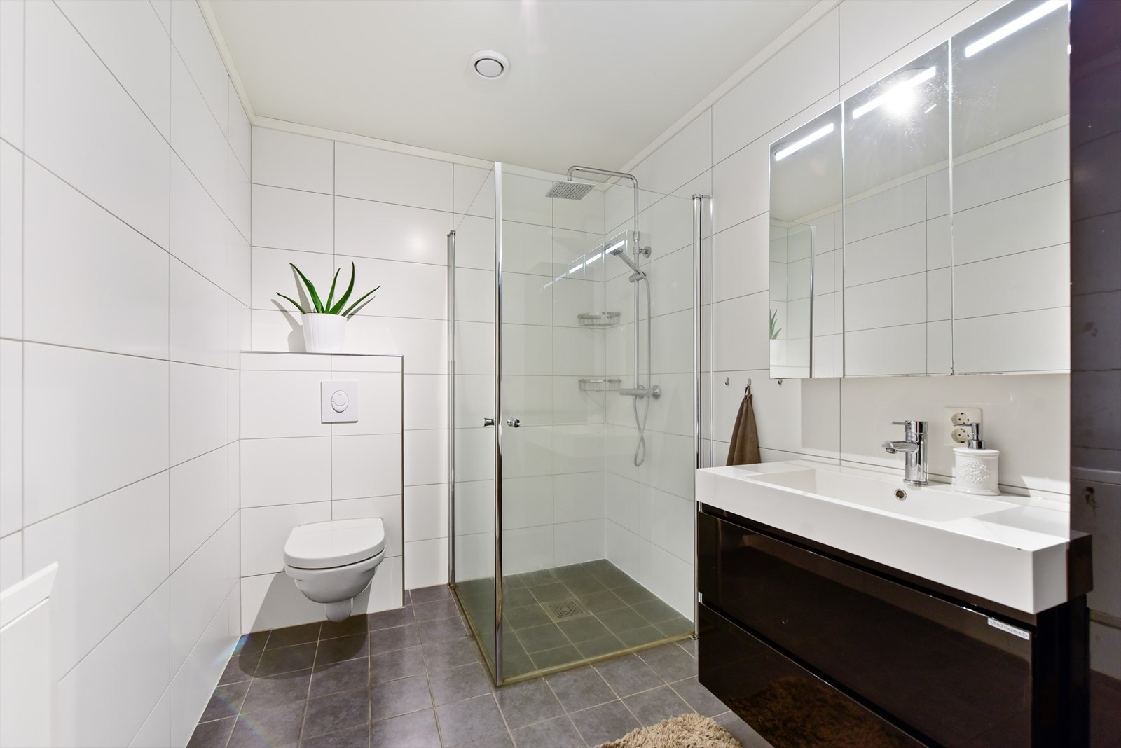 Flislagt bad med vegghengt toalett og dusjhjørne med innfellbare glassdører Galleribilde