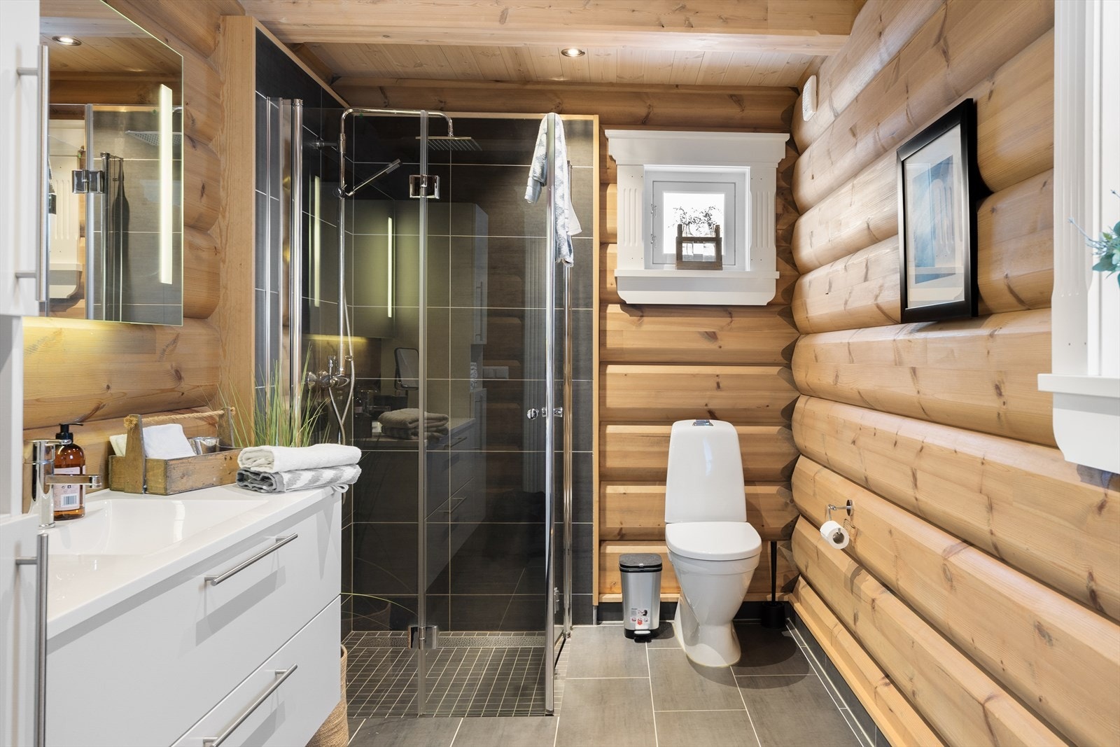 Badet inneholder toalett, dusjhjørne og innredning med servang og høyskap med gode oppbevaringsmuligheter Galleribilde