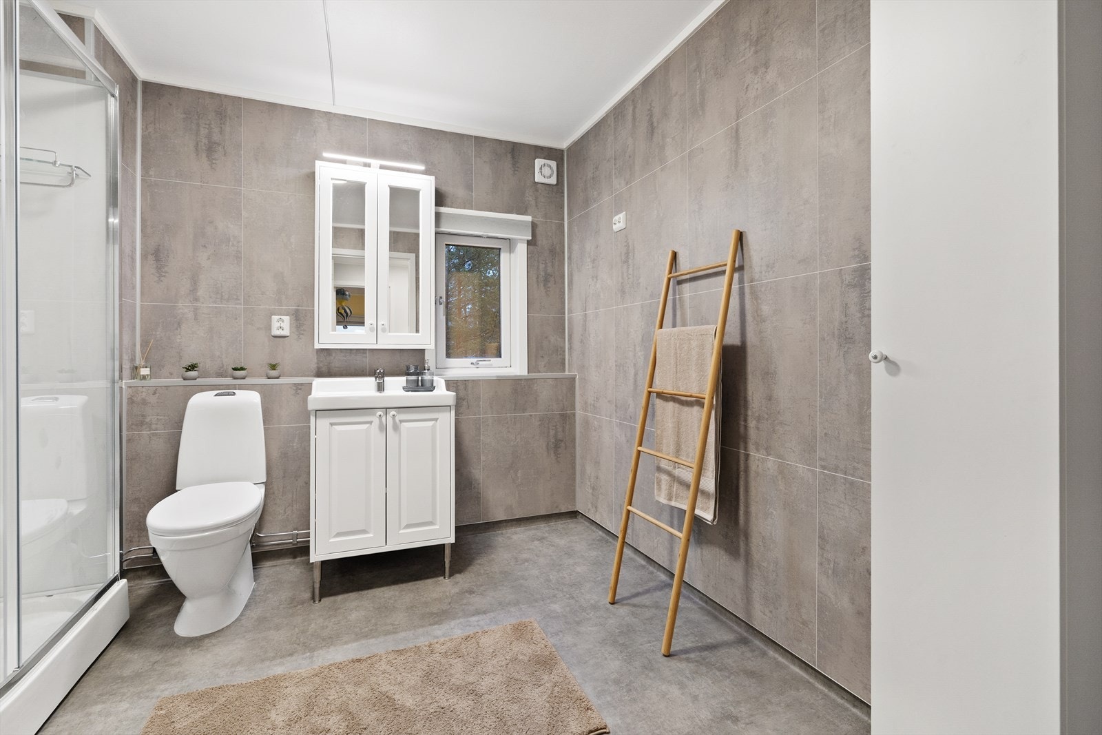 Badet består av servant med underskap, speilskap med belysning, toalett, dusjkabinett og opplegg for vaskemaskin. Galleribilde