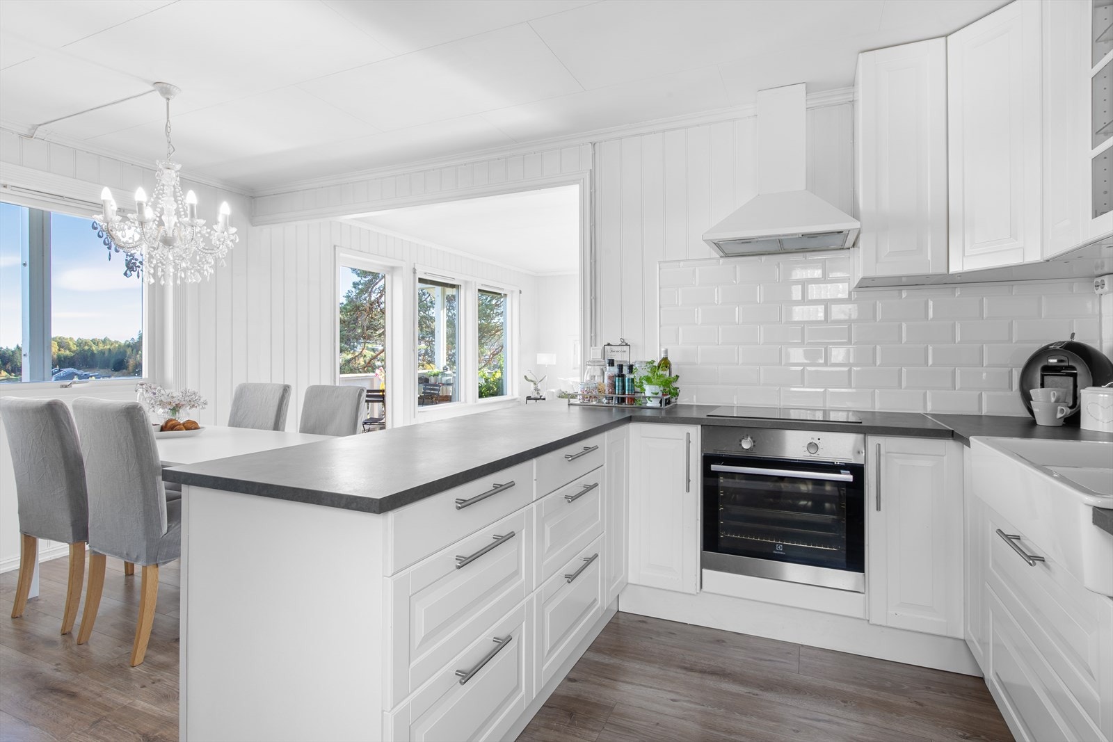 Klassisk kjøkken med klarer linjer mellom de hvite profilerte frontene, grå benkeplate og detaljer i stål. Galleribilde