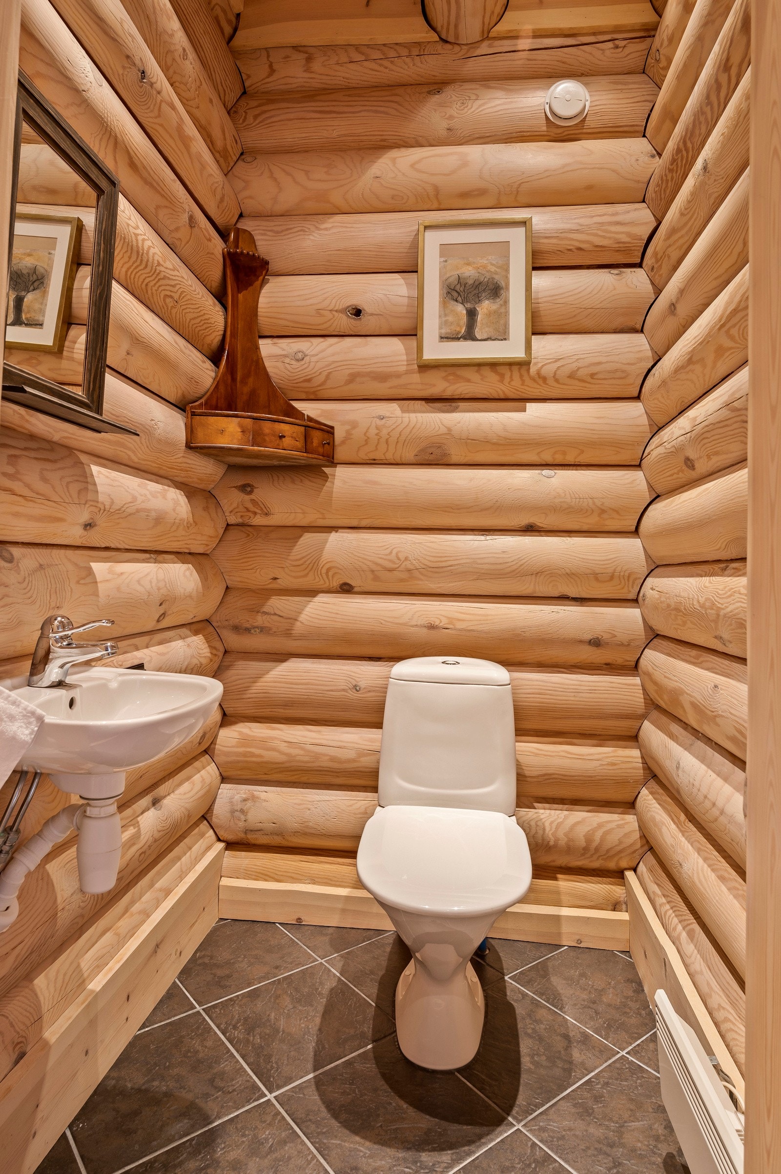 Flislagt toalettrom innredet med gulvstående toalett, vegghengt servant samt speil på vegg over servant. Galleribilde