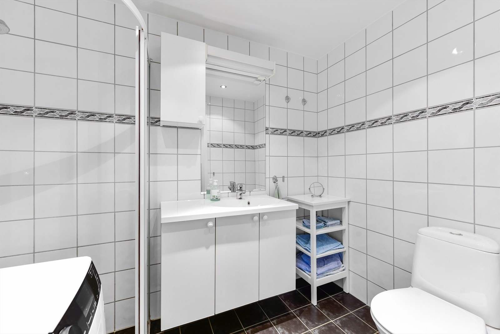 Flislagt bad, innredet med servantskap, frittstående toalett, dusjnisje og opplegg for vaskemaskin Galleribilde