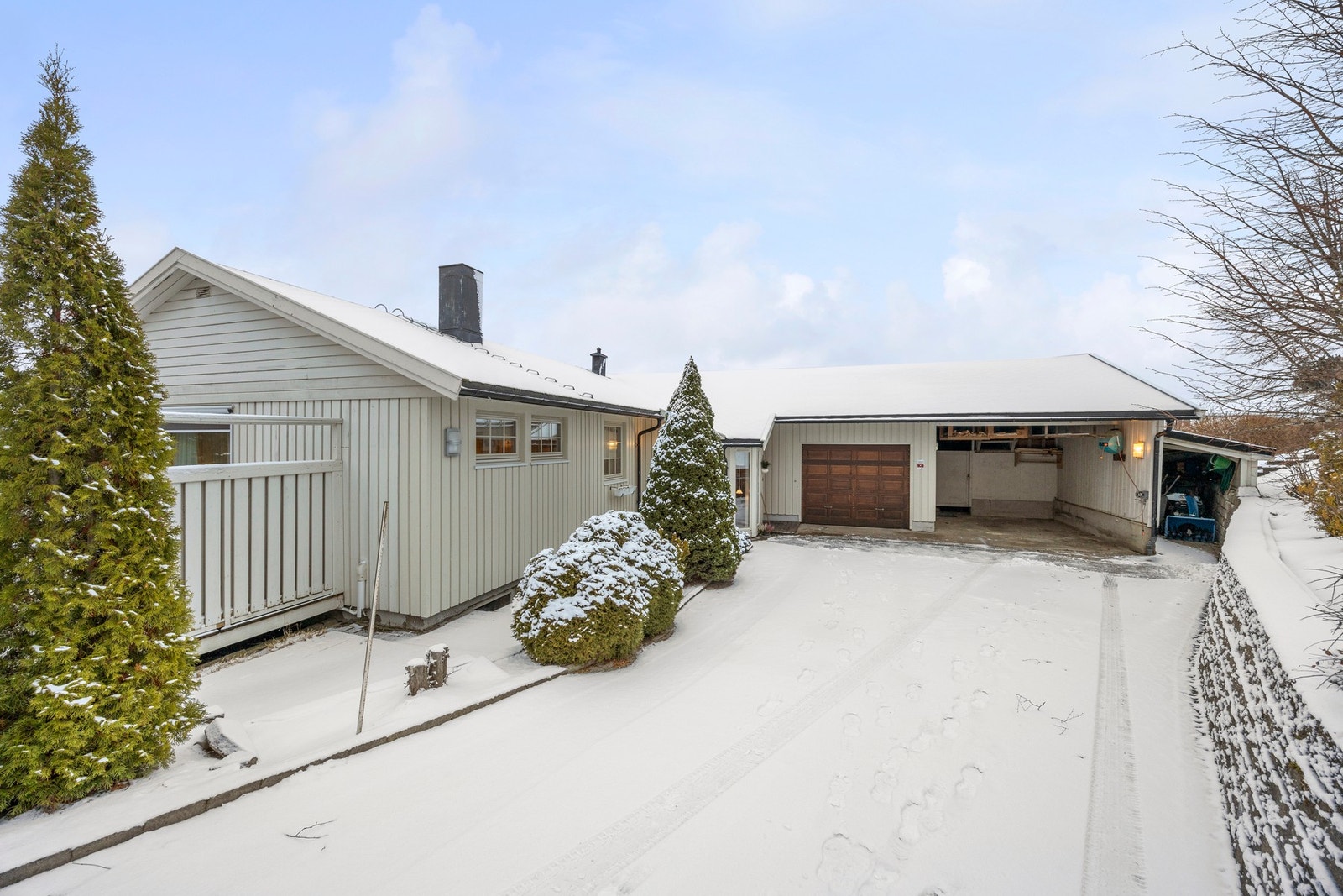 Under snøen skjuler det seg en steinbelagt gårdsplass. Vegg mot parkeringsplassen fikk etterisolering, ny vindsperre og kledning i 2025 Galleribilde