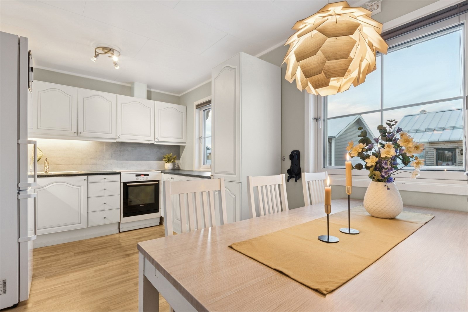 Kjøkkenet har en tidløs innredning med lysmalte profilerte fronter, laminert benkeplate med dobbel stålvask og fliser på vegg over benk. Galleribilde