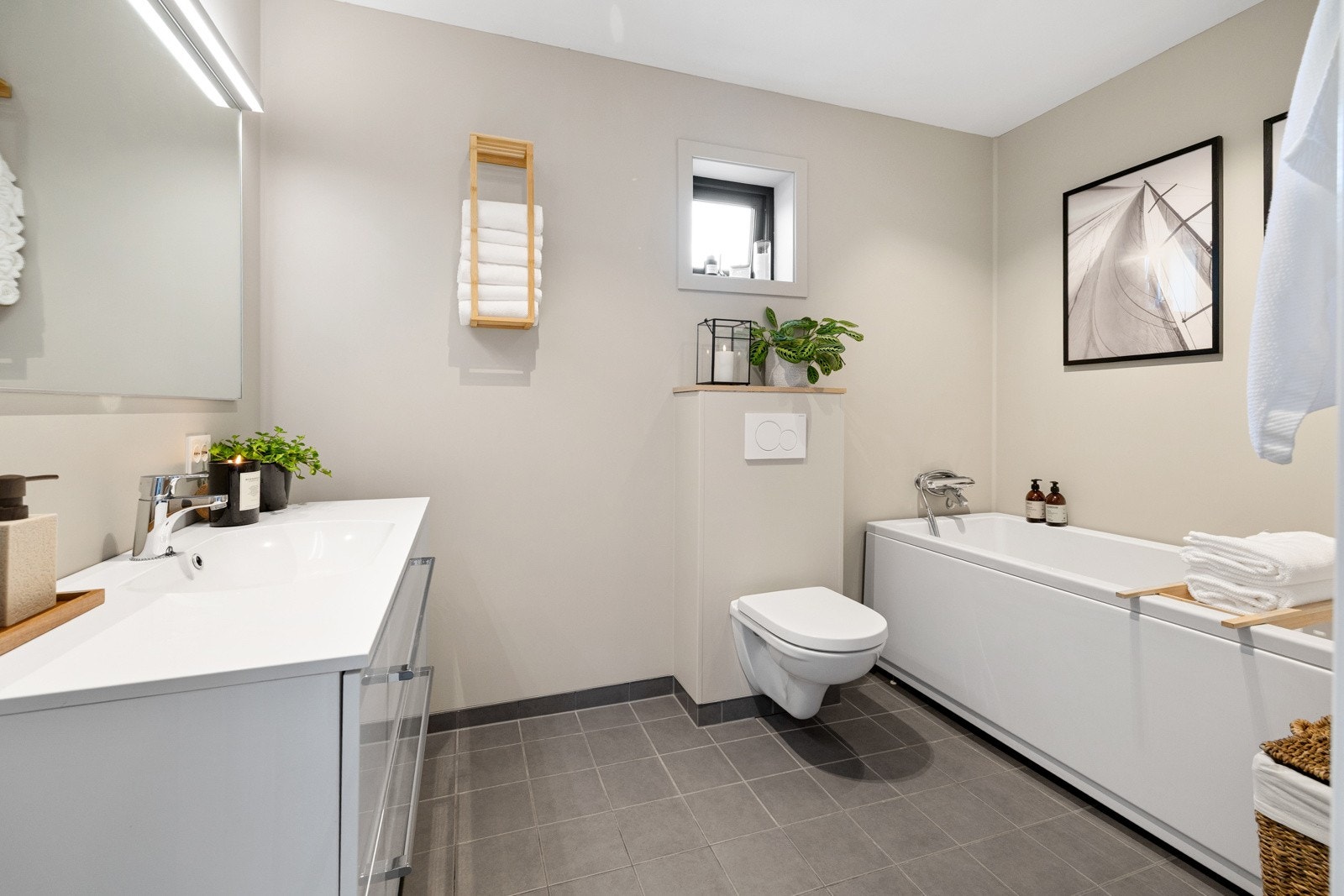 Badet i første etasje har fliser på gulvet og vårtomsplater på vegg. Her er innredning med servant, speil med lys, vegghengt toalett - Galleribilde