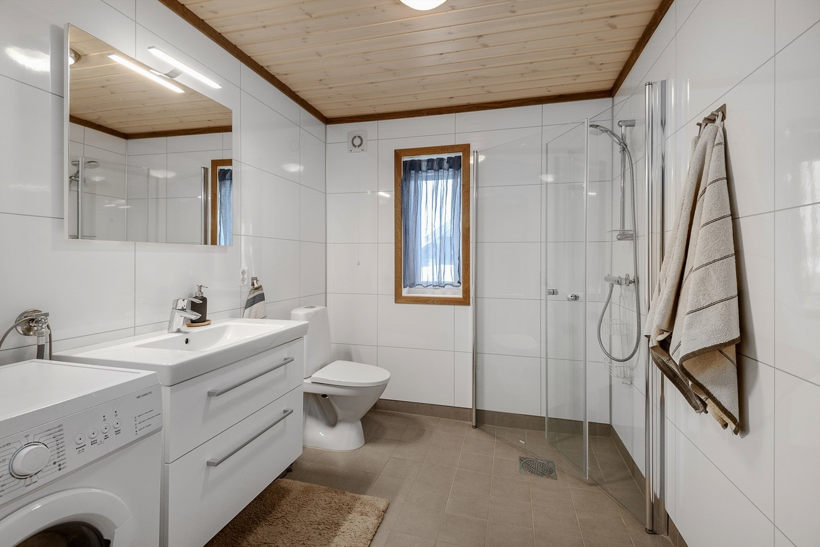 Stilrent og praktisk bad med dusjhjørne, WC, servantinnredning og opplegg for vaskemaskin. Galleribilde