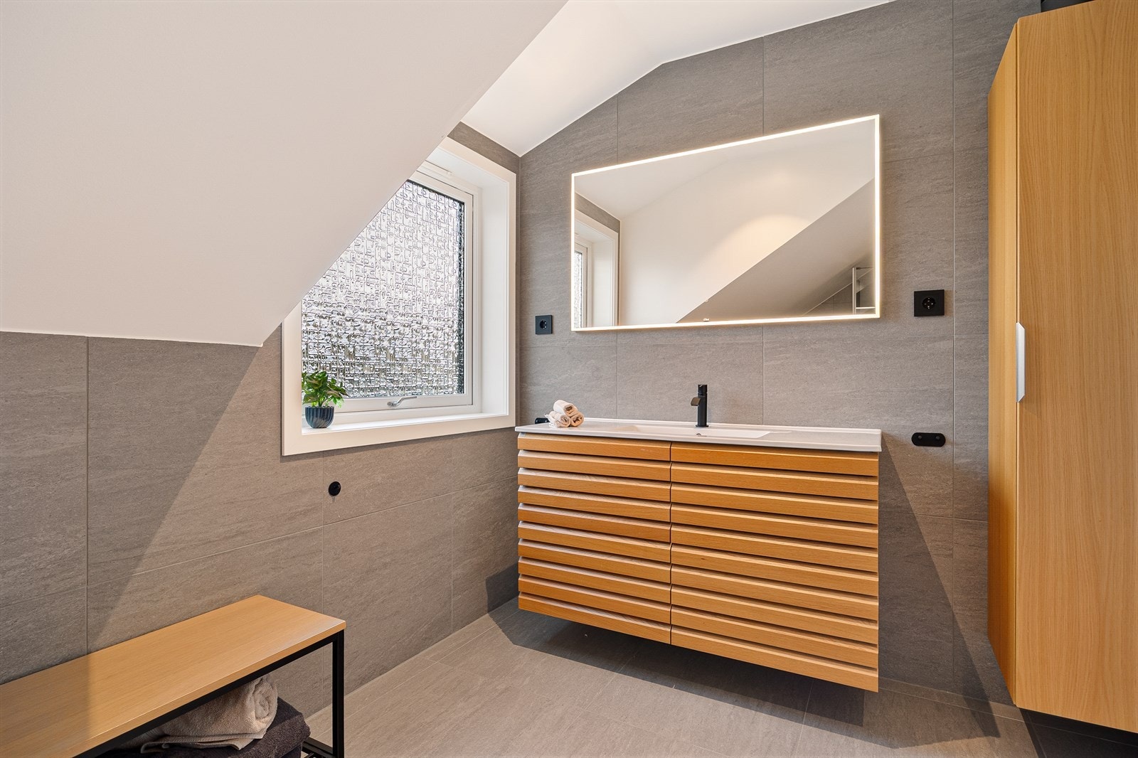 Badet er gjennomført med fine grå fliser på gulv og vegger, servant og skap i eik. Galleribilde