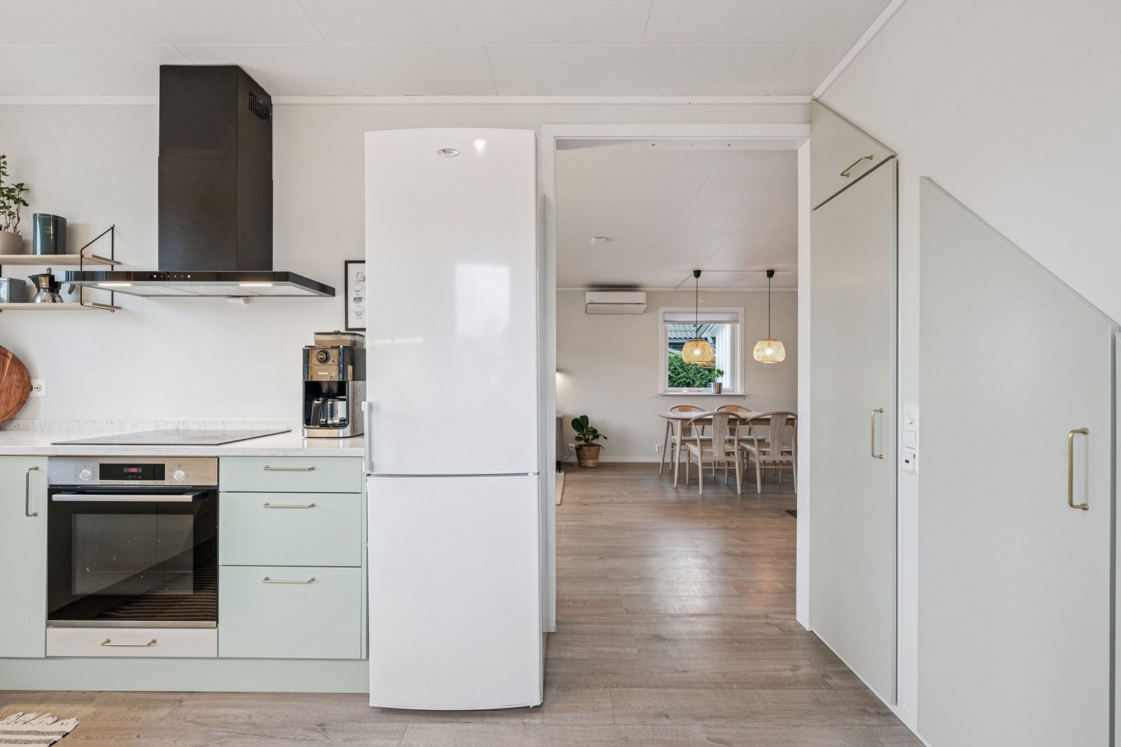 Plassen under trappen er smart utnyttet med en plassbygd løsning som rommer fryseskap og uttrekkbare skap, og gir rikelig med lagringsplass. Galleribilde