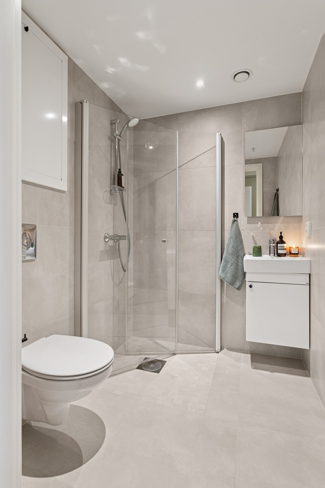 Badet er utstyrt med en dusj med innfellbare glassvegger, en innredning med heldekkende servant og et vegghengt toalett med skjult sisterne. Galleribilde