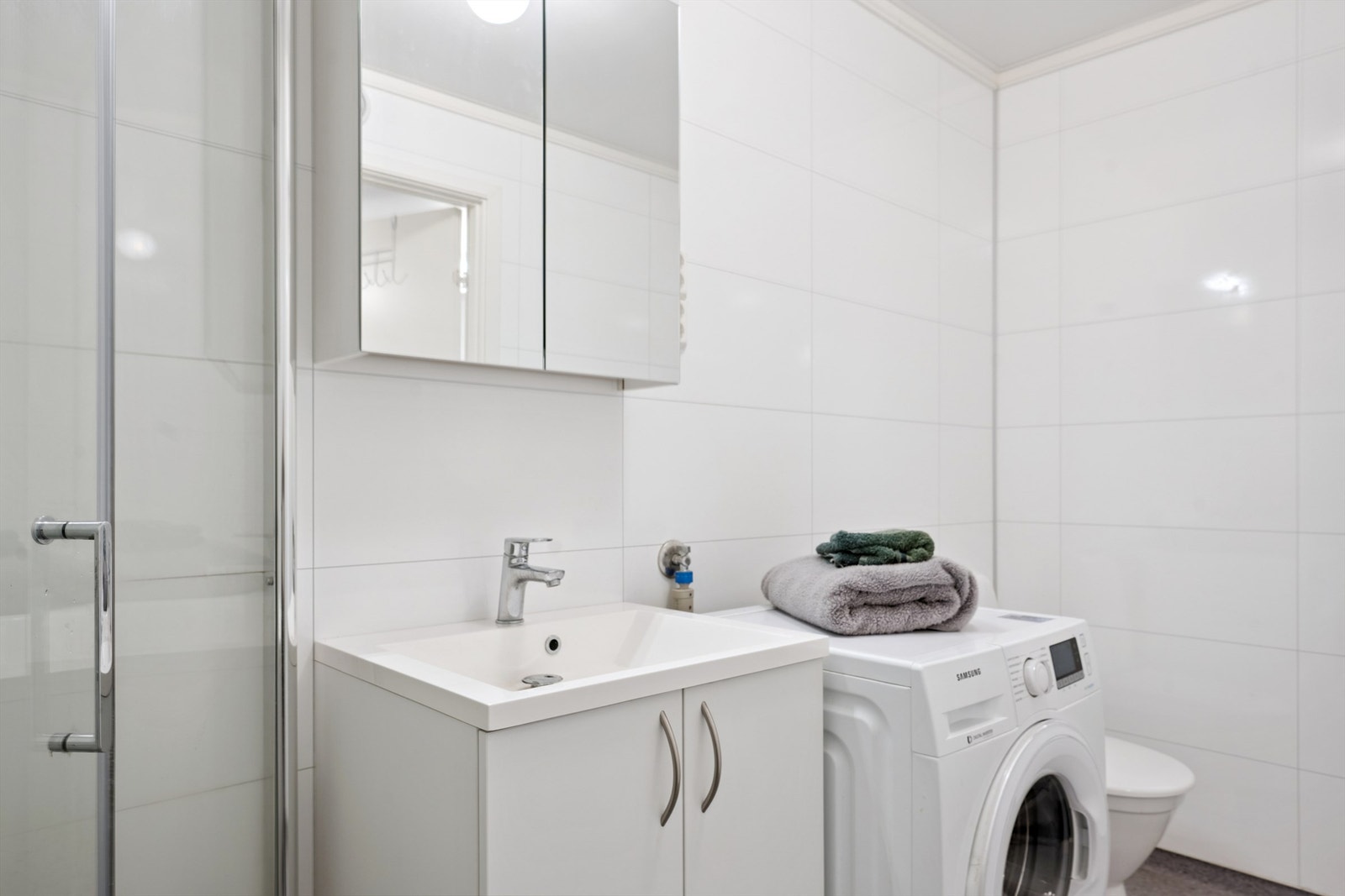 Baderomsinnredning med servant og speilskap, samt dusjhjørne med innfellbare dører. Galleribilde