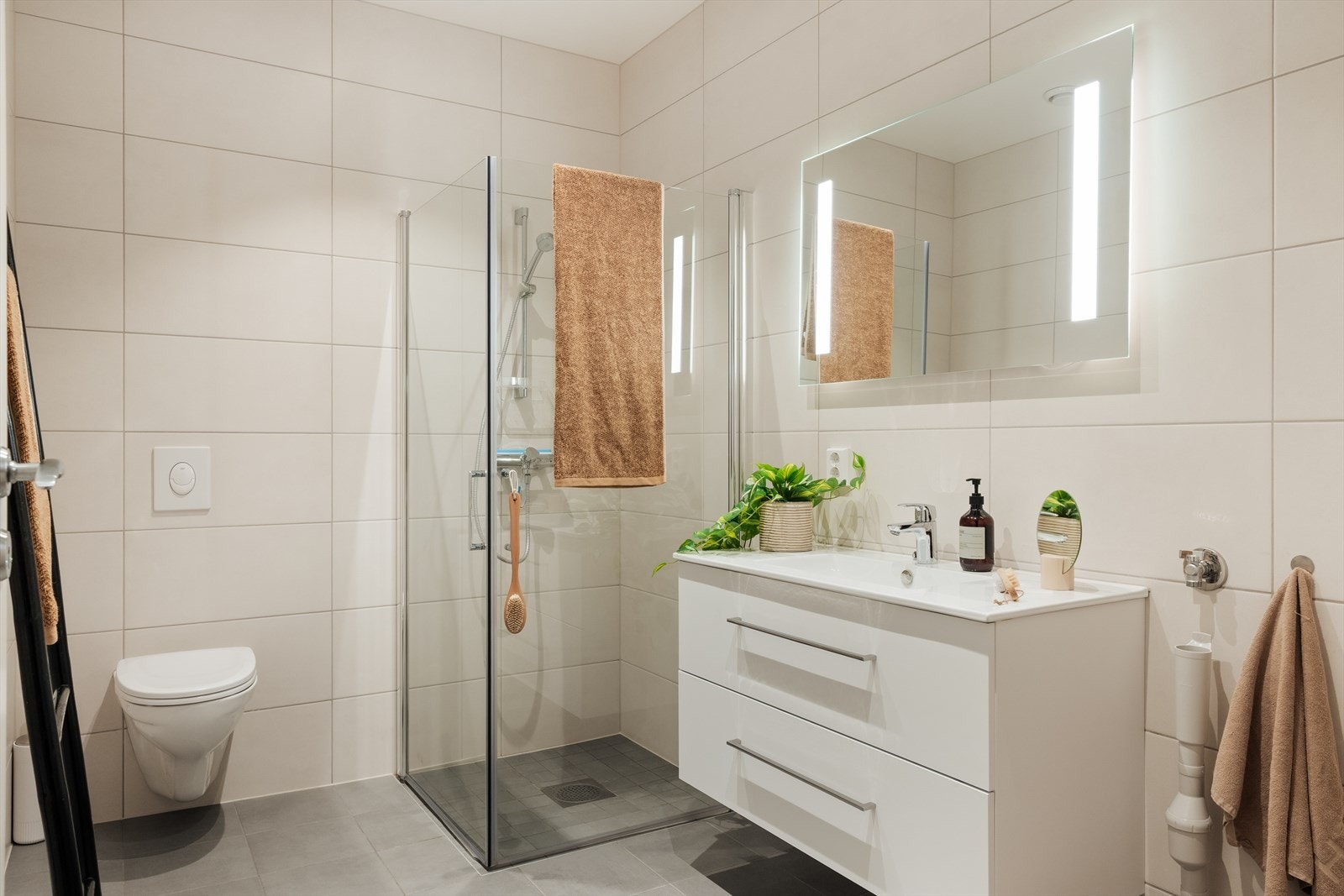 Helfliset og moderne bad, utstyrt med vegghengt toalett, helstøpt servant med skuffer, dusjvegger i klart glass og opplegg for vaskemaskin Galleribilde